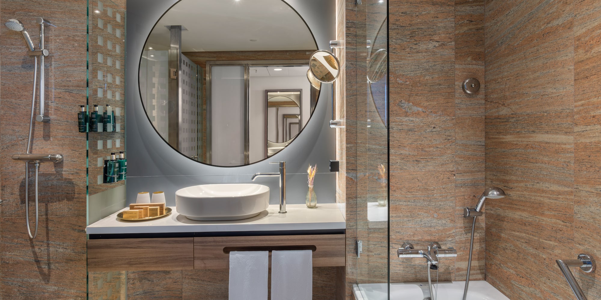 Baño moderno con espejo circular, lavabo, ducha y bañera. Granito.