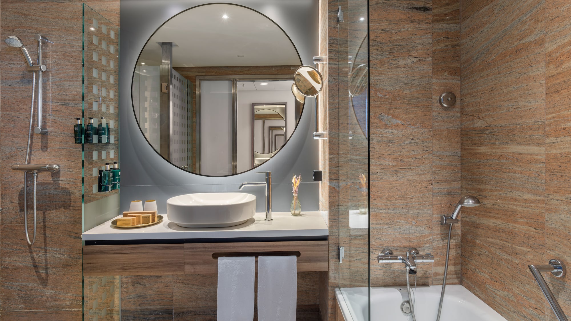 Baño moderno con espejo circular, lavabo, ducha y bañera. Granito.
