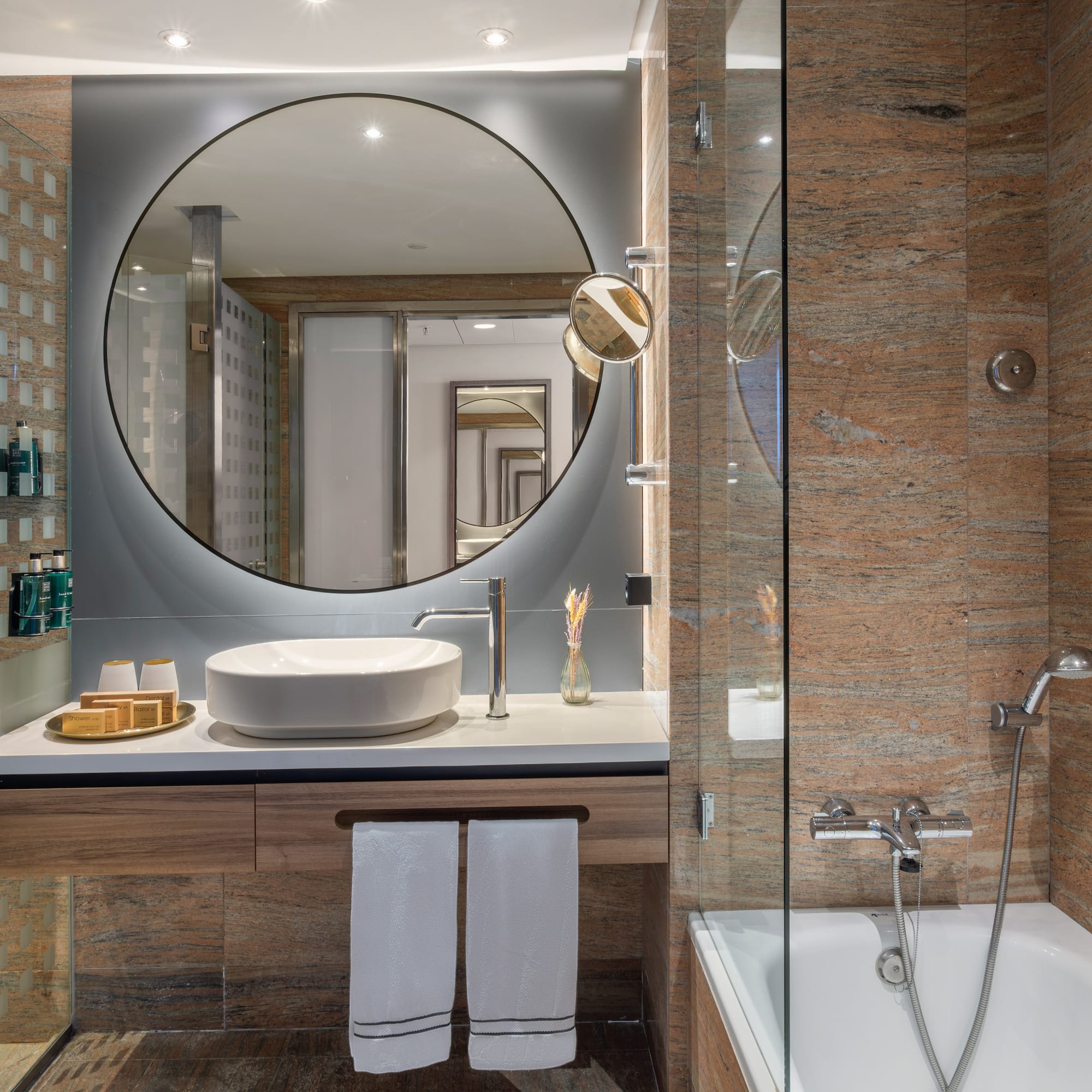 Baño moderno con espejo circular, lavabo, ducha y bañera. Granito.