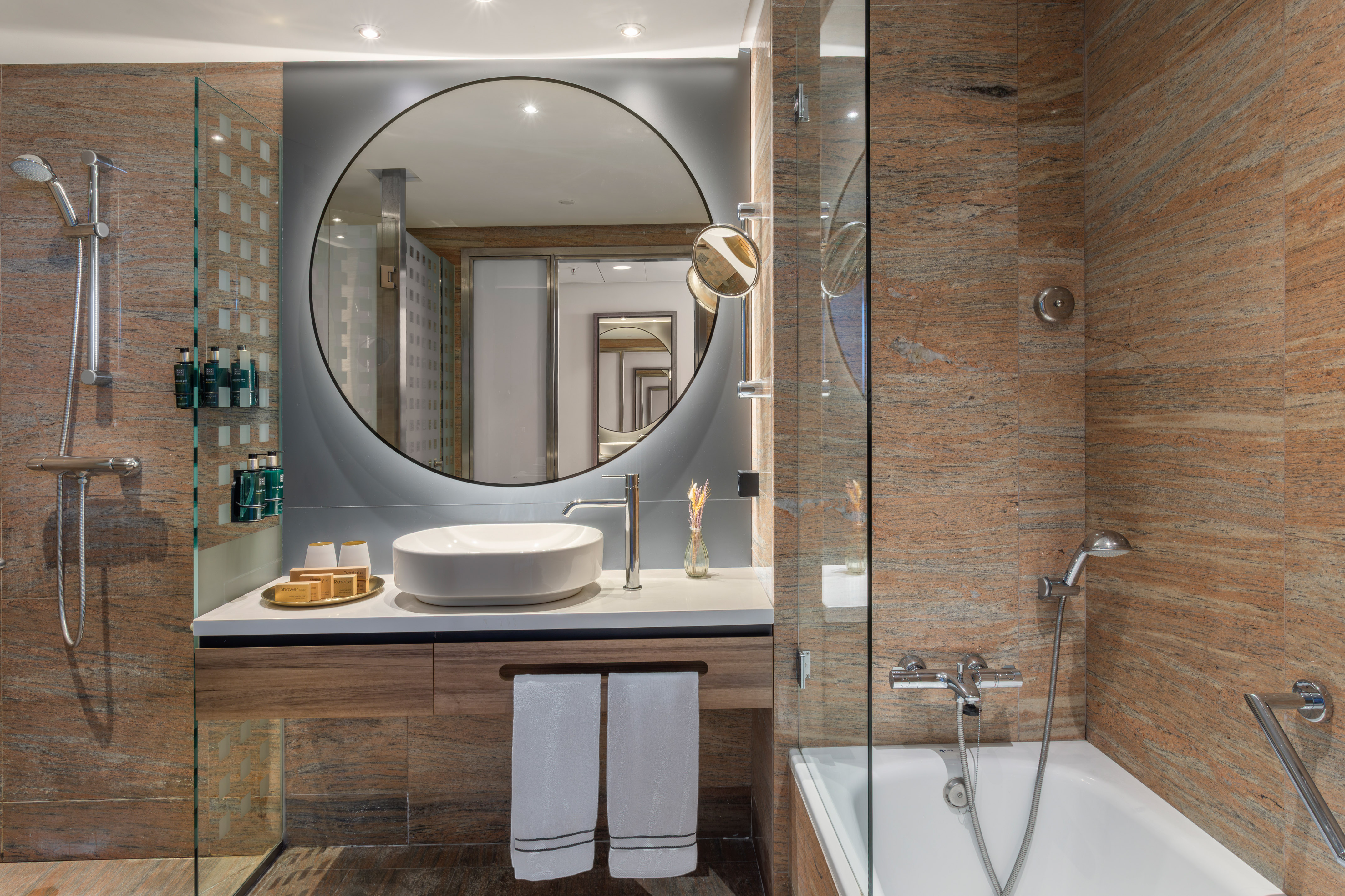 Baño moderno con espejo circular, lavabo, ducha y bañera. Granito.