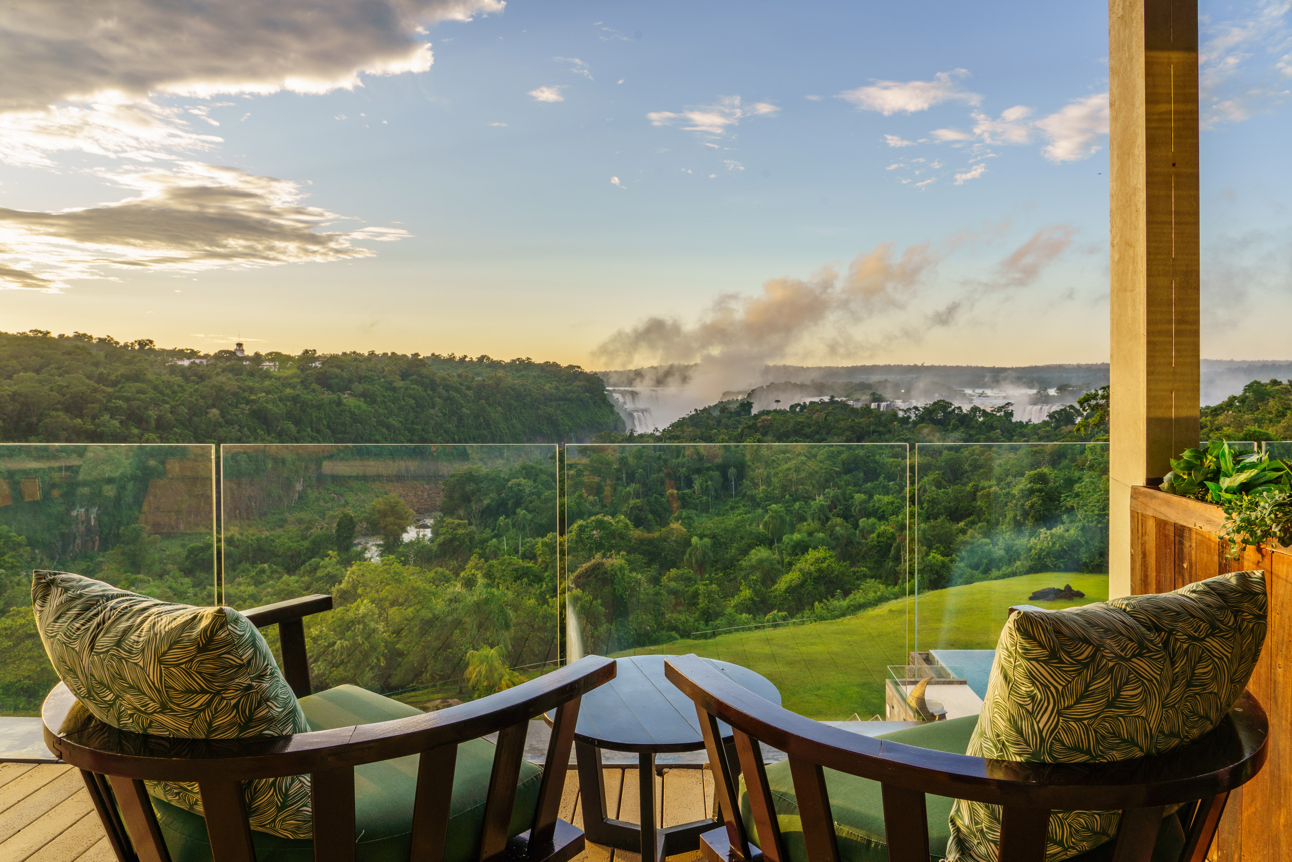 Balcony chairs overlooking Iguazu Falls at sunset with dense jungle.
