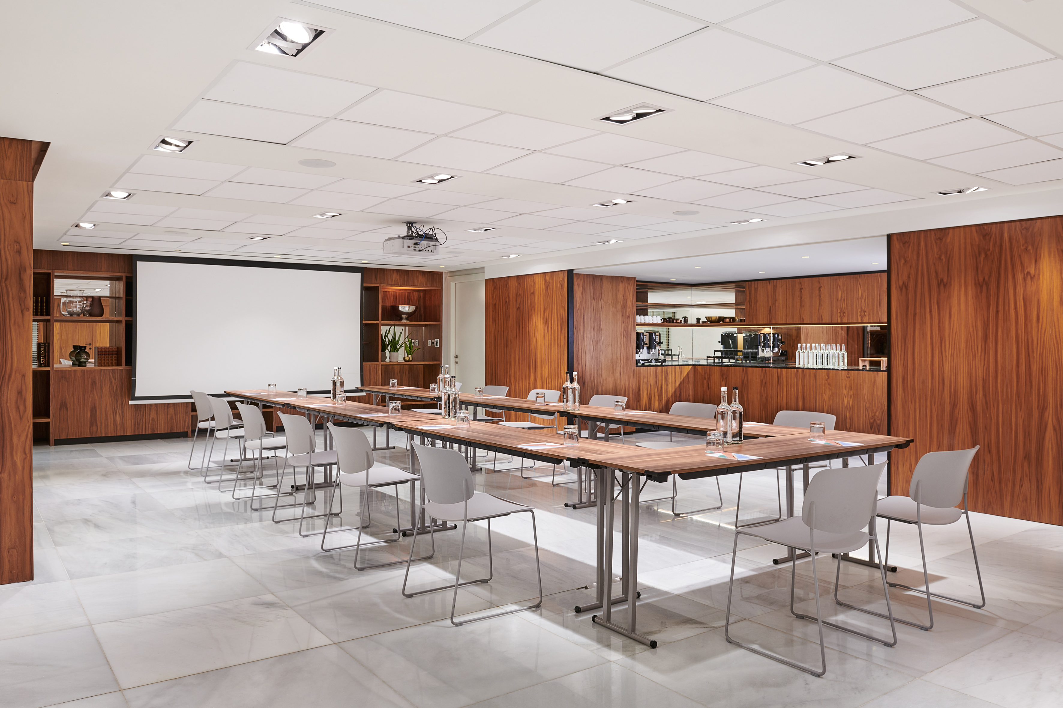 Corporate meeting room with U-table setup, projector screen, and modern wood paneling.