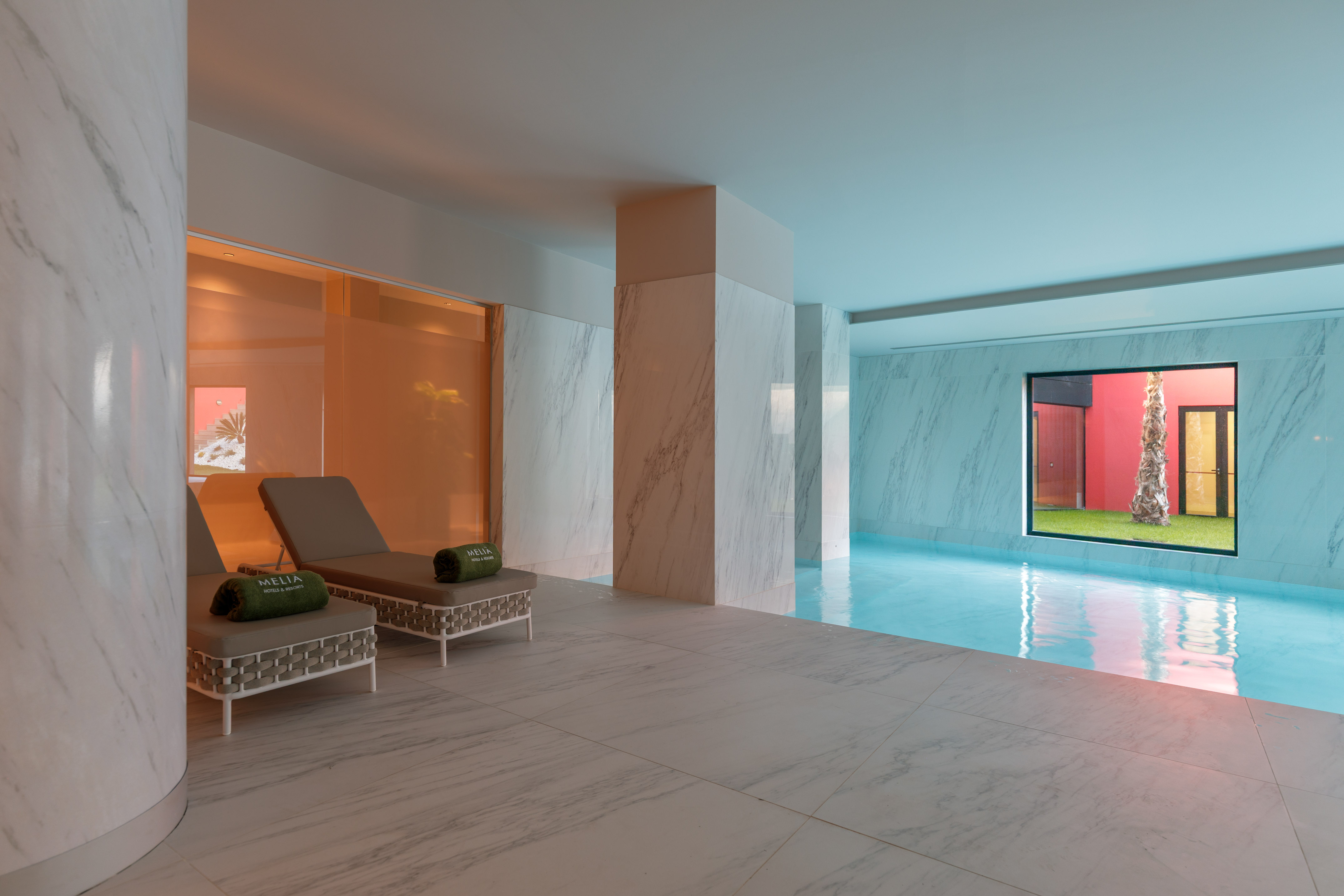 Meliã hotel indoor pool with marble, sun loungers, and tropical palm view.