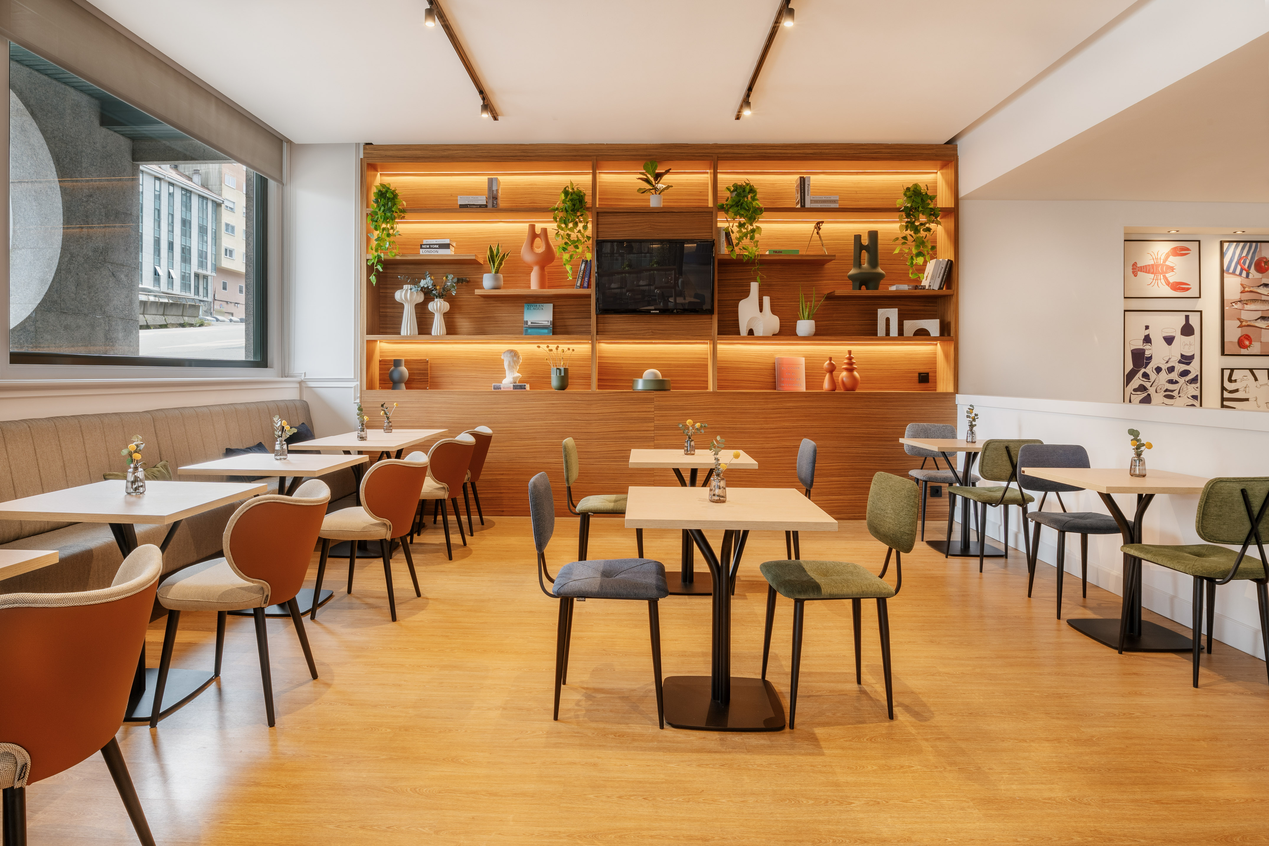 Cafetería moderna con estantería iluminada, mesas y sillas de diseño.