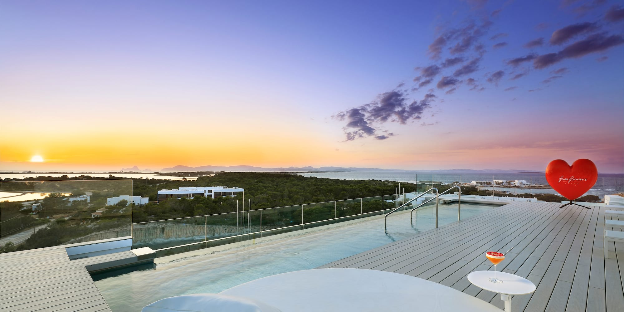 a pool with a table and chairs on a deck with a view of the ocean
