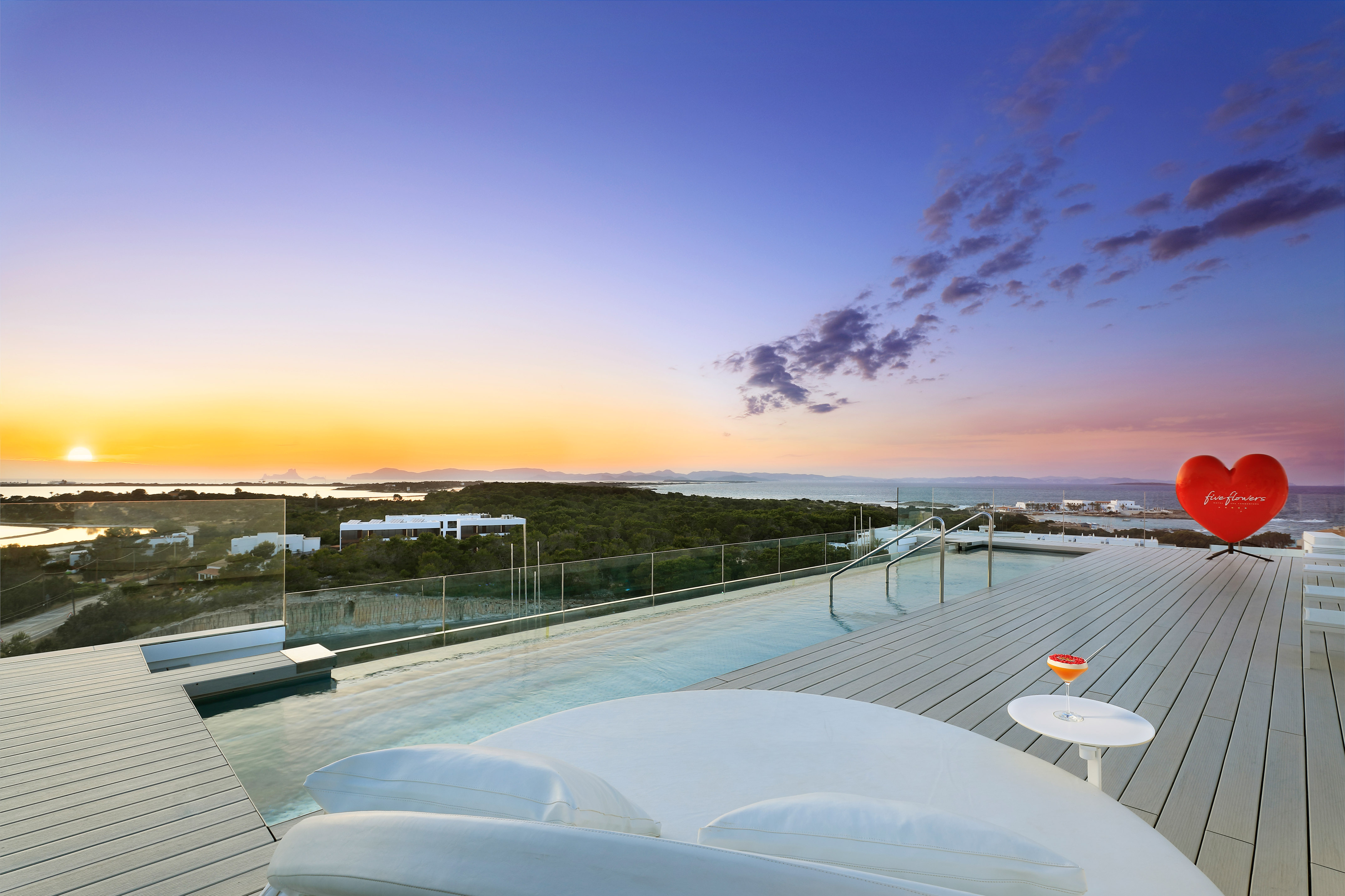 Sunset over rooftop infinity pool, ocean view, lounge, cocktail, red heart.