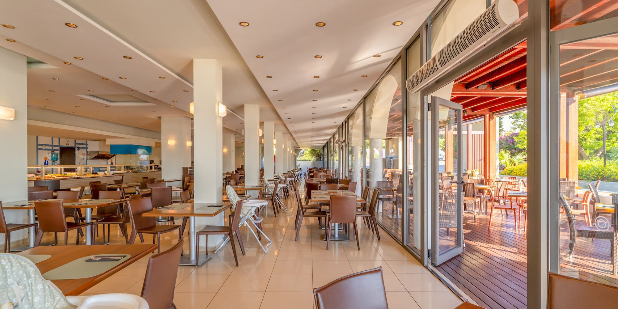 Spacious resort restaurant with buffet, indoor tables, and sunny outdoor terrace.