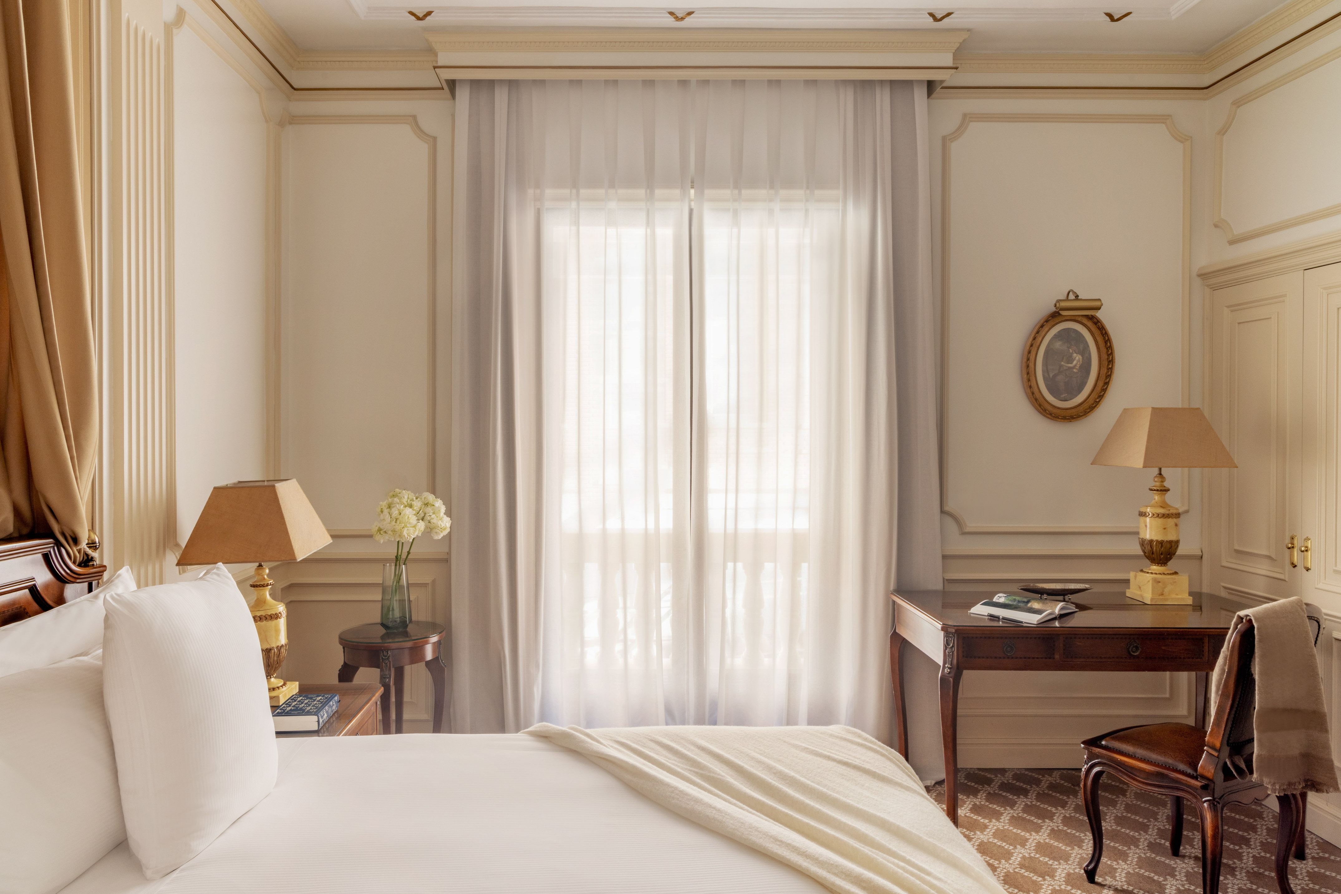 Luxury hotel bedroom with elegant furnishings, white bed, and bright window.