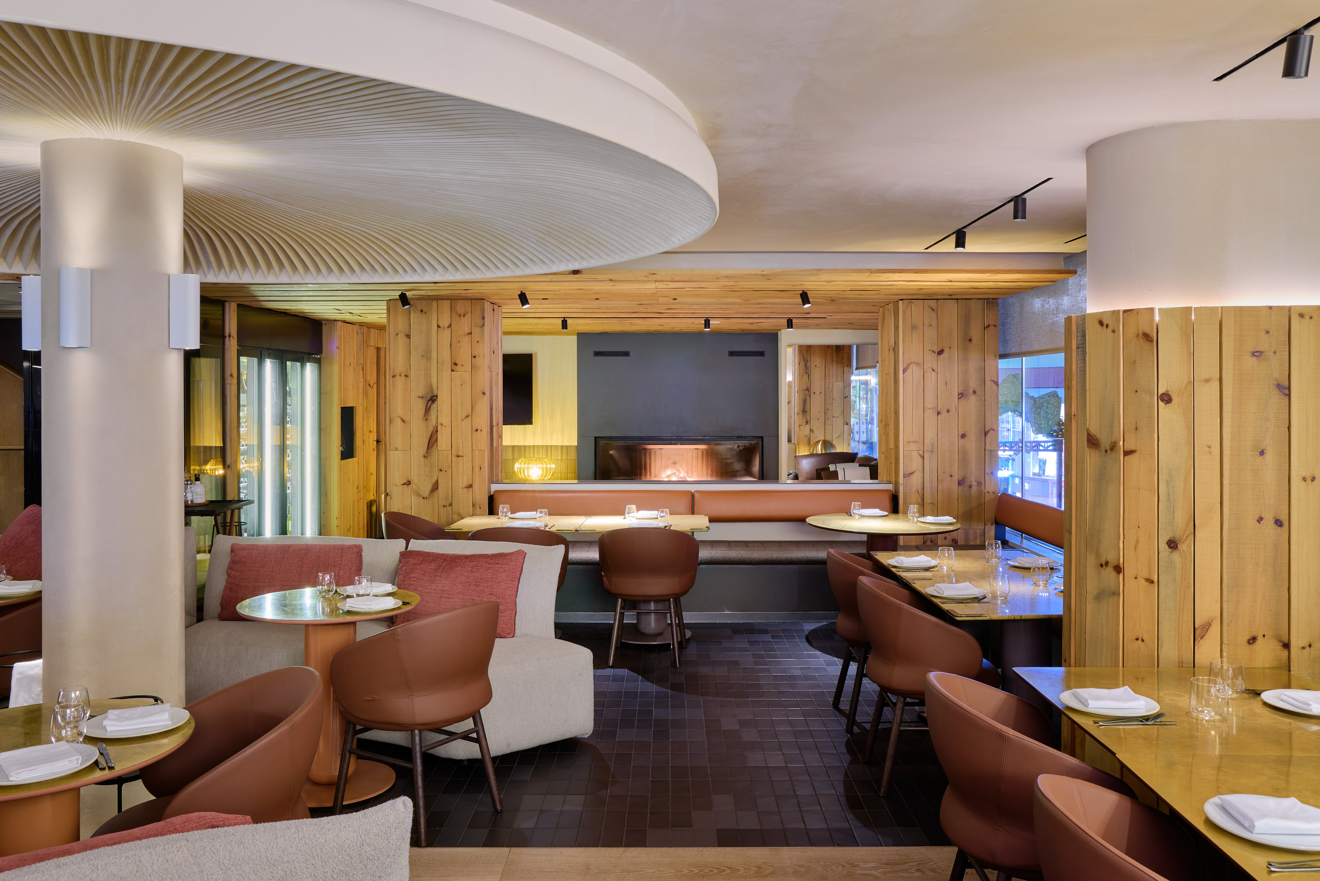 Modern restaurant interior: wood walls, brown chairs, fireplace, ribbed ceiling.