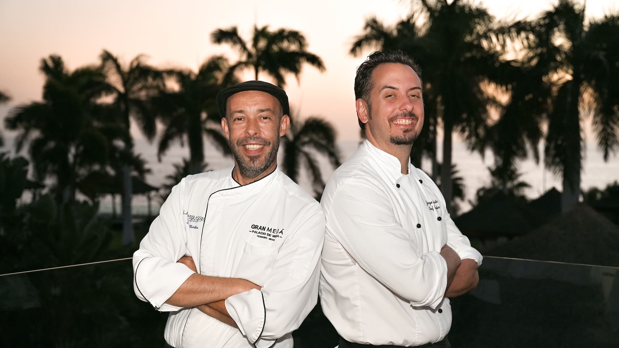 Smiling chefs from Gran Meliá Tenerife resort, standing before palm trees.