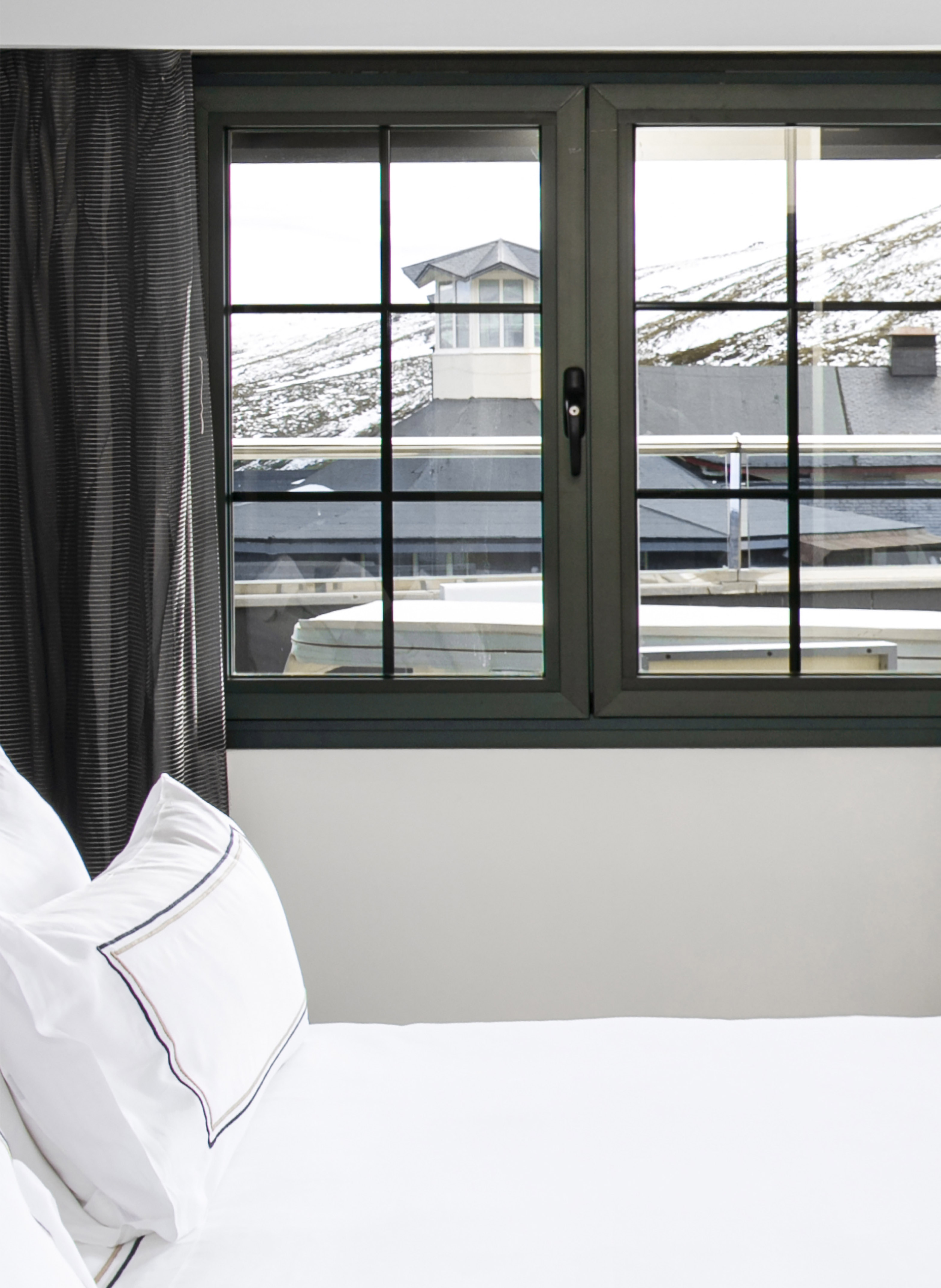 White bed by window, snowy mountain village view, dark curtain.