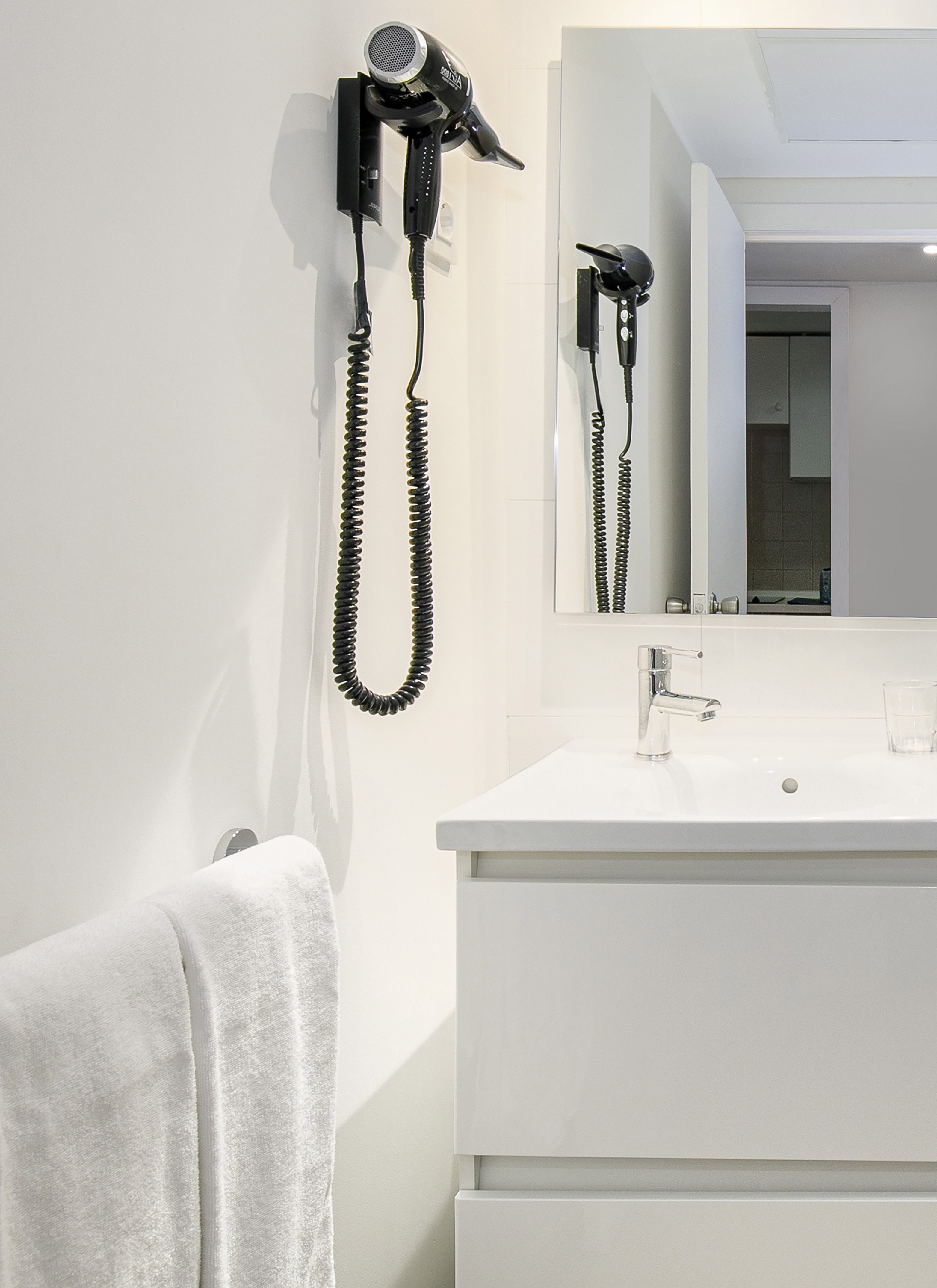 Wall-mounted hairdryer, white vanity, sink, and mirror in a modern bathroom.