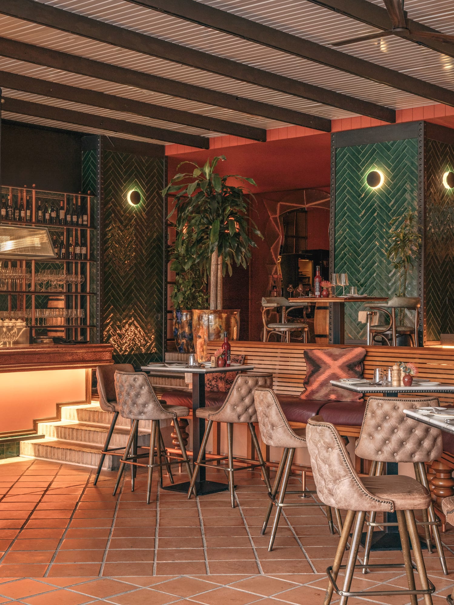 Restaurant interior with green herringbone tiles, warm lighting, terracotta floor.