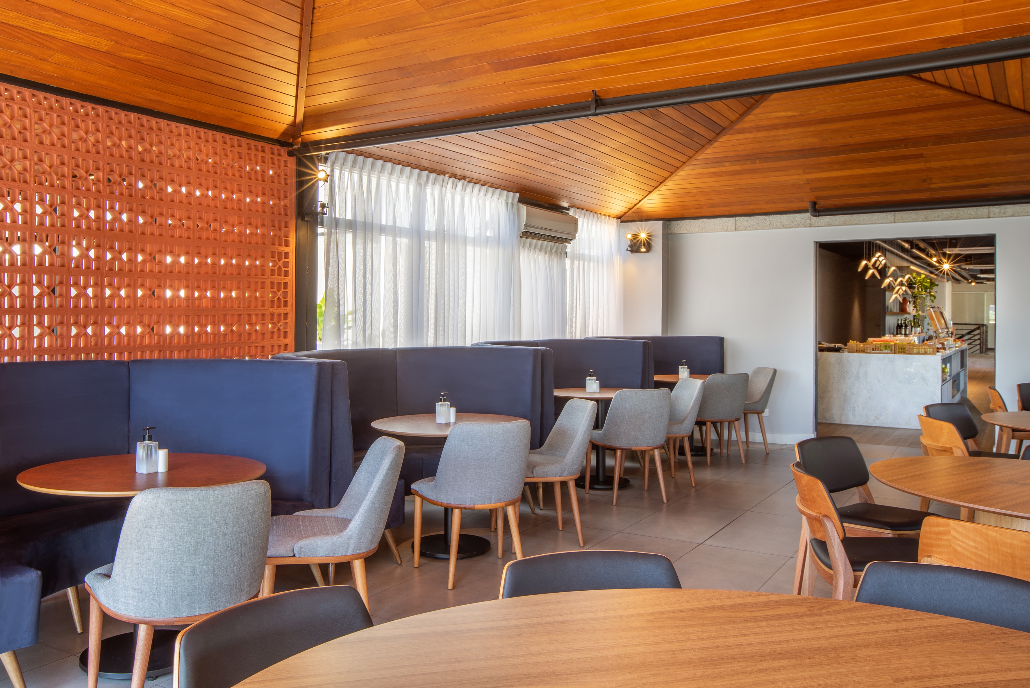 Modern restaurant dining area with wooden ceiling, blue booths, and orange accent wall.
