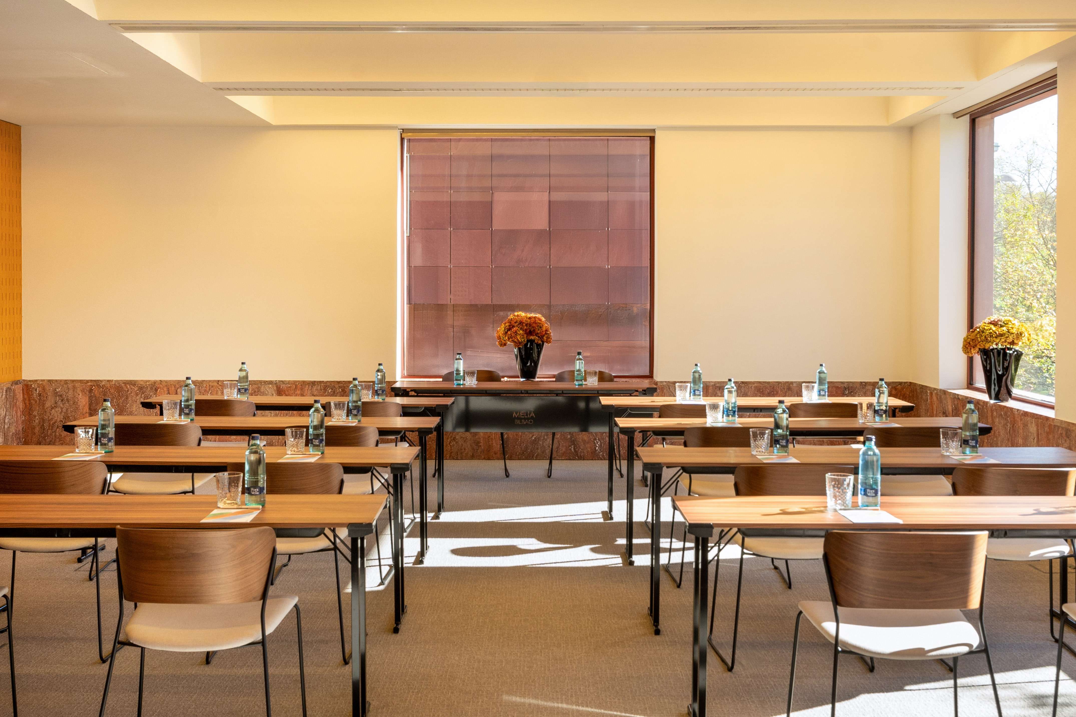 Conference room with classroom setup, individual water bottles, and bright windows.
