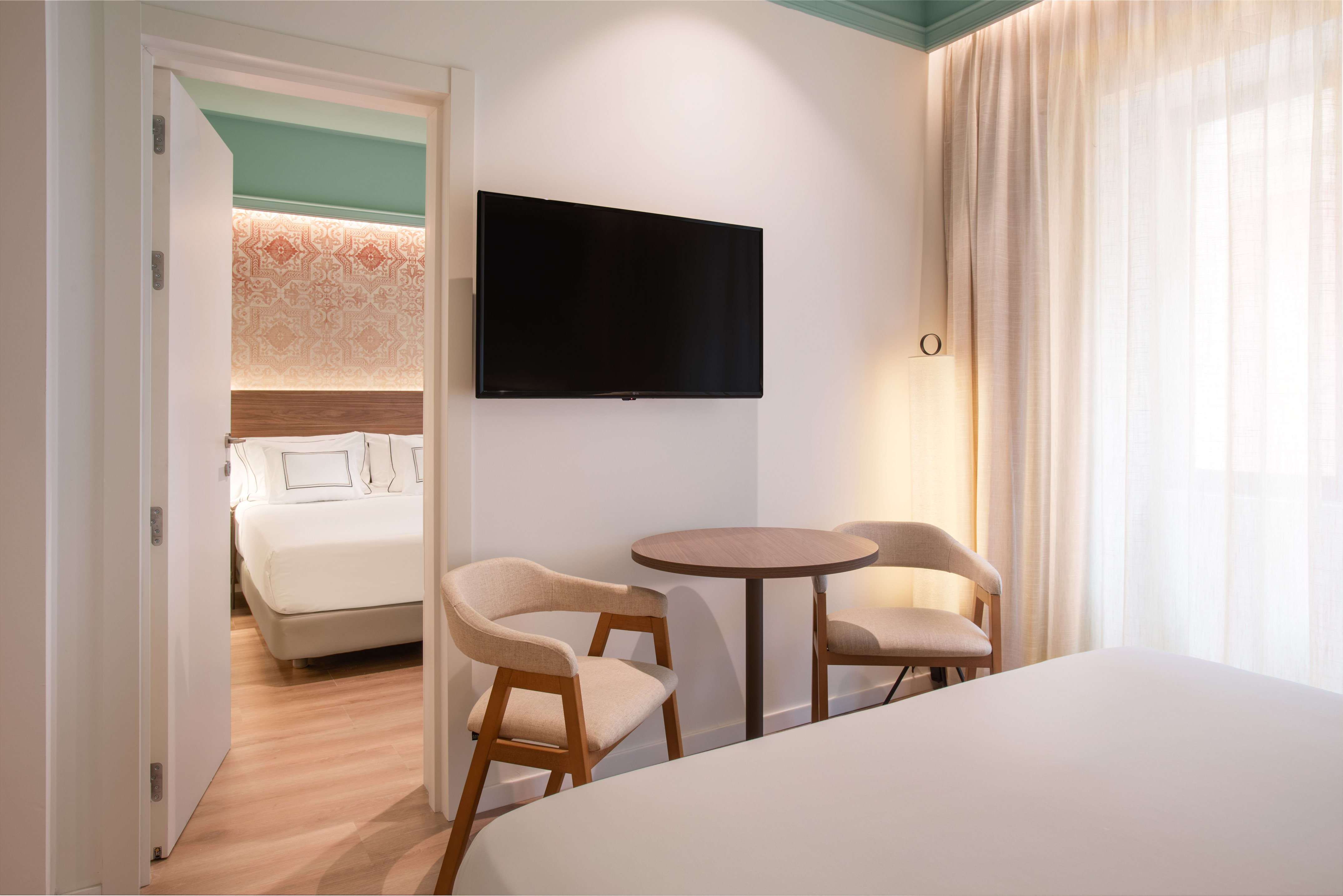 Modern hotel room with TV, sitting area, and adjoining bedroom.