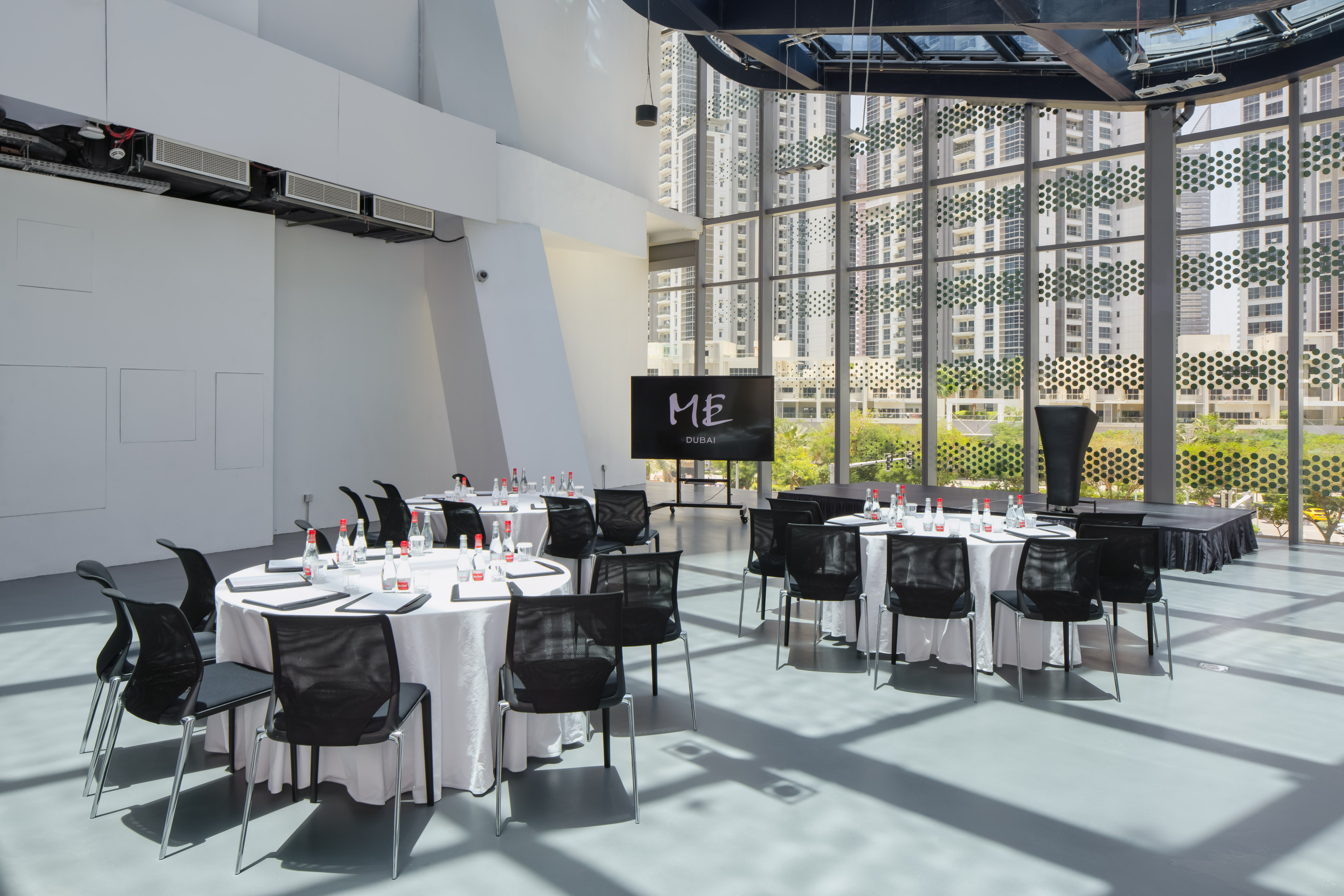 Bright Dubai meeting space with round tables, 'ME' screen, and city views.