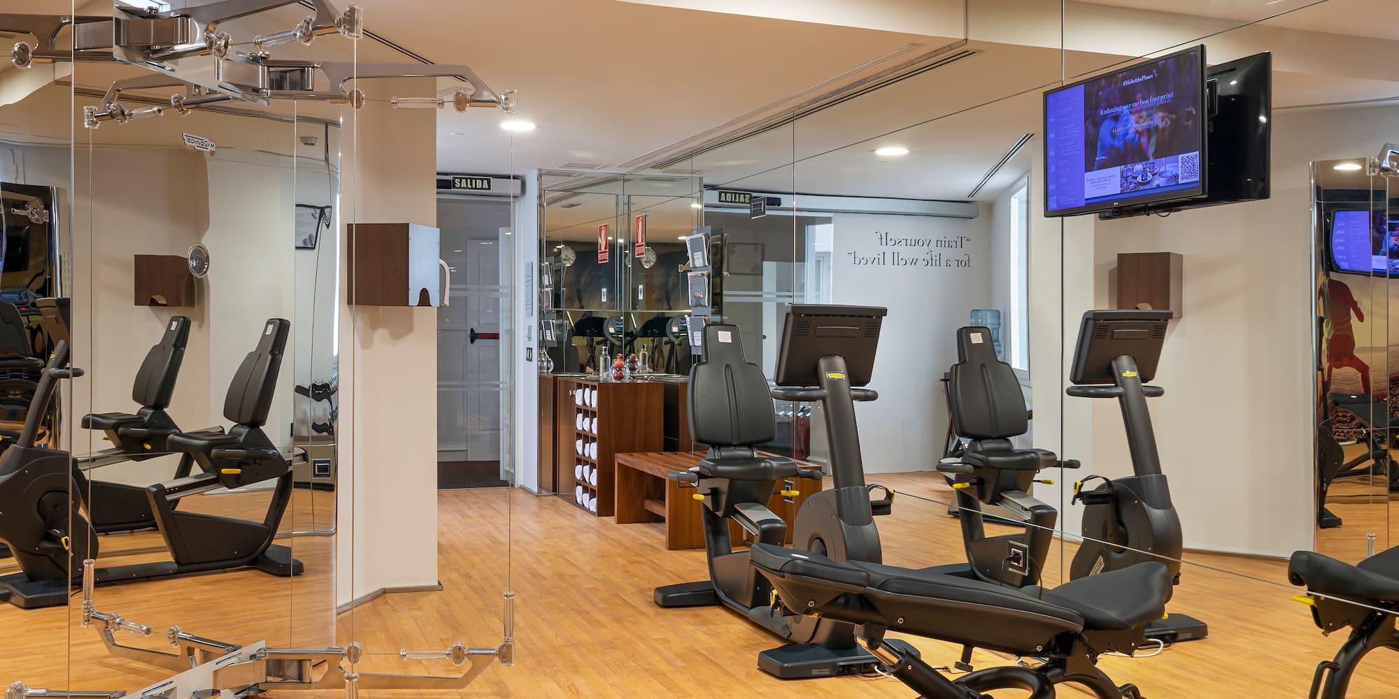 Modern hotel gym with Technogym cardio machines, mirrored walls, and wood floor.