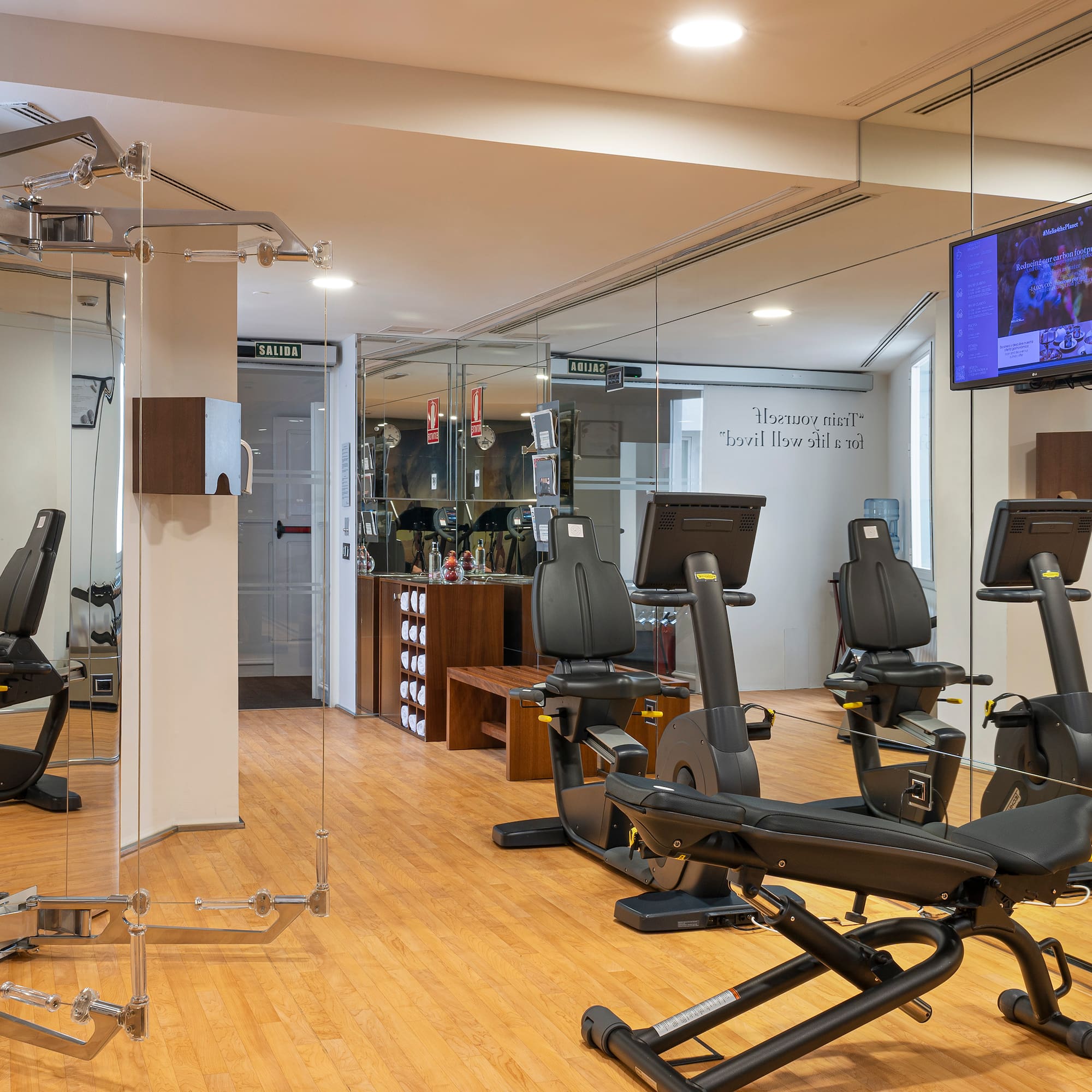Modern hotel gym with Technogym cardio machines, mirrored walls, and wood floor.