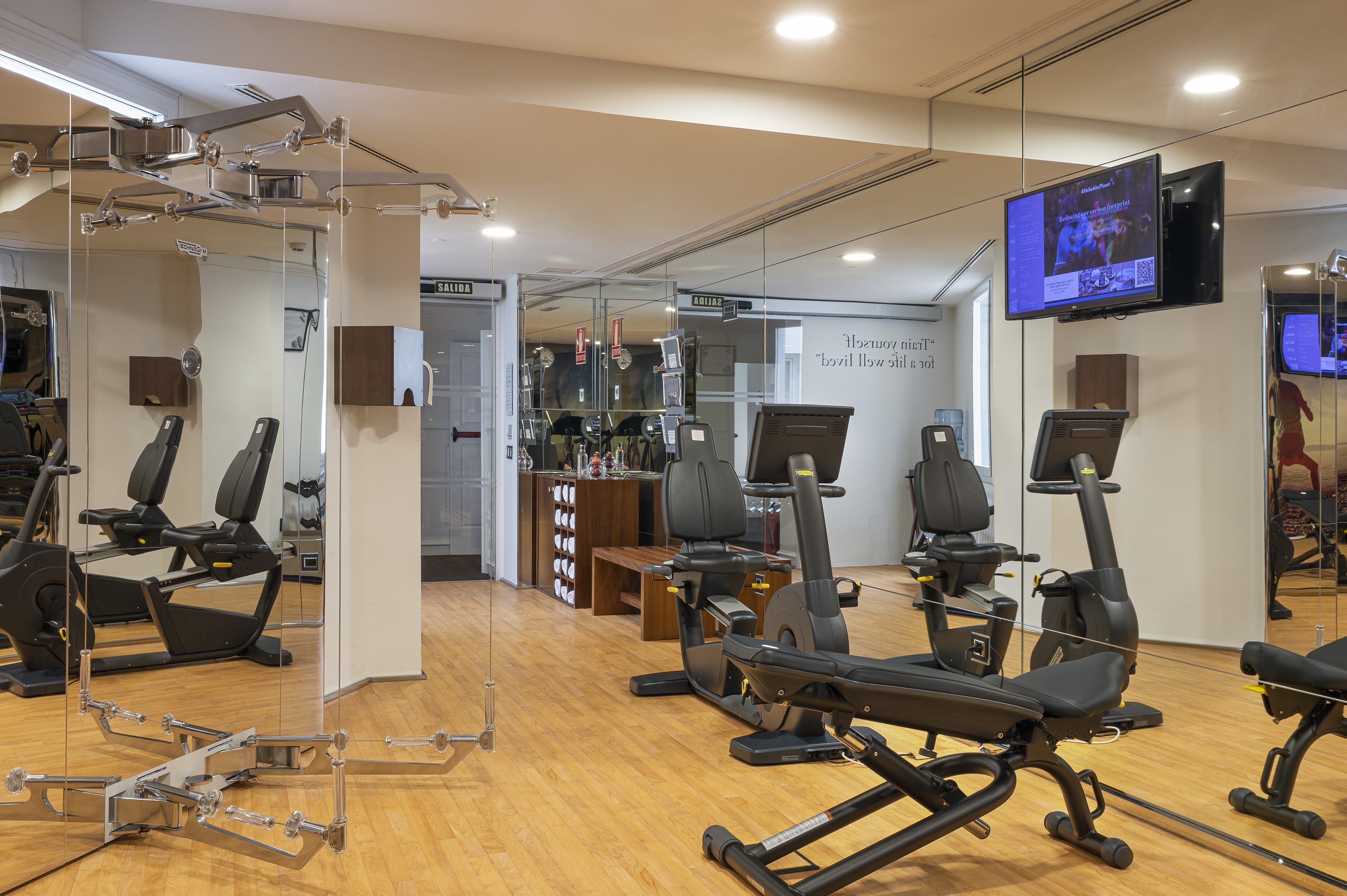 Modern hotel gym with Technogym cardio machines, mirrored walls, and wood floor.