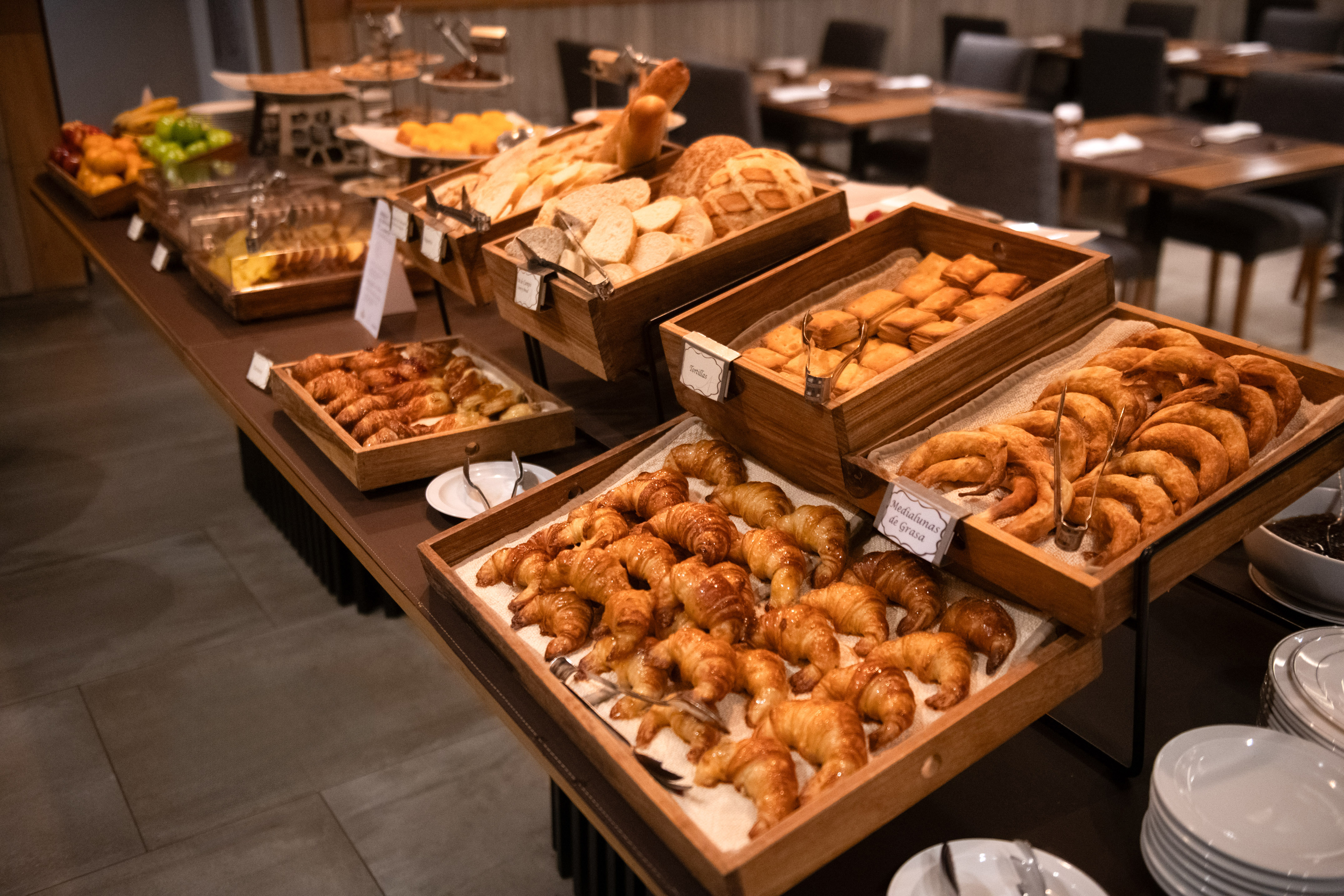 Breakfast buffet with croissants, pastries, bread, and fruit on wooden displays.