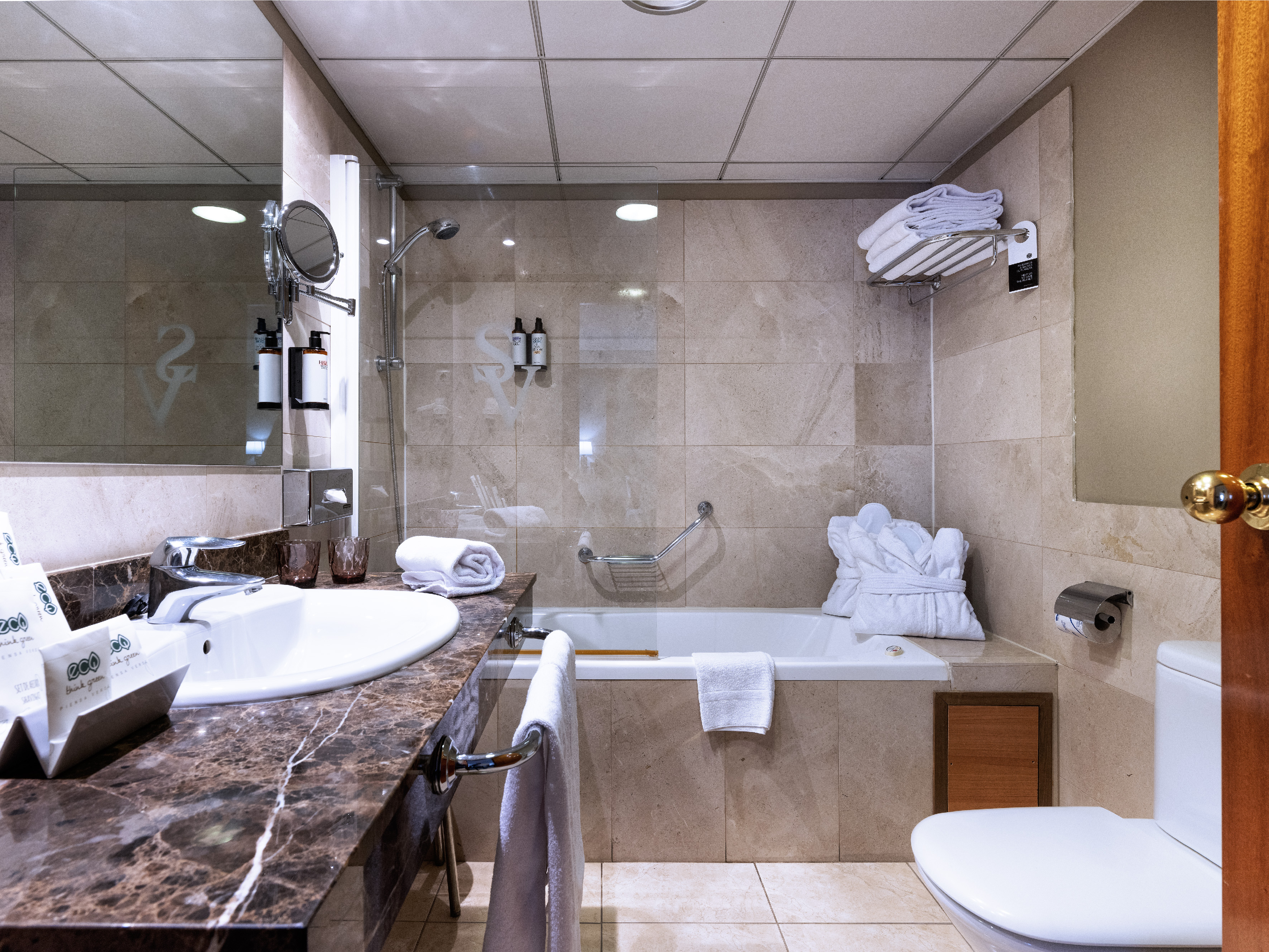 Modern hotel bathroom with shower, bathtub, toilet, and marble vanity.