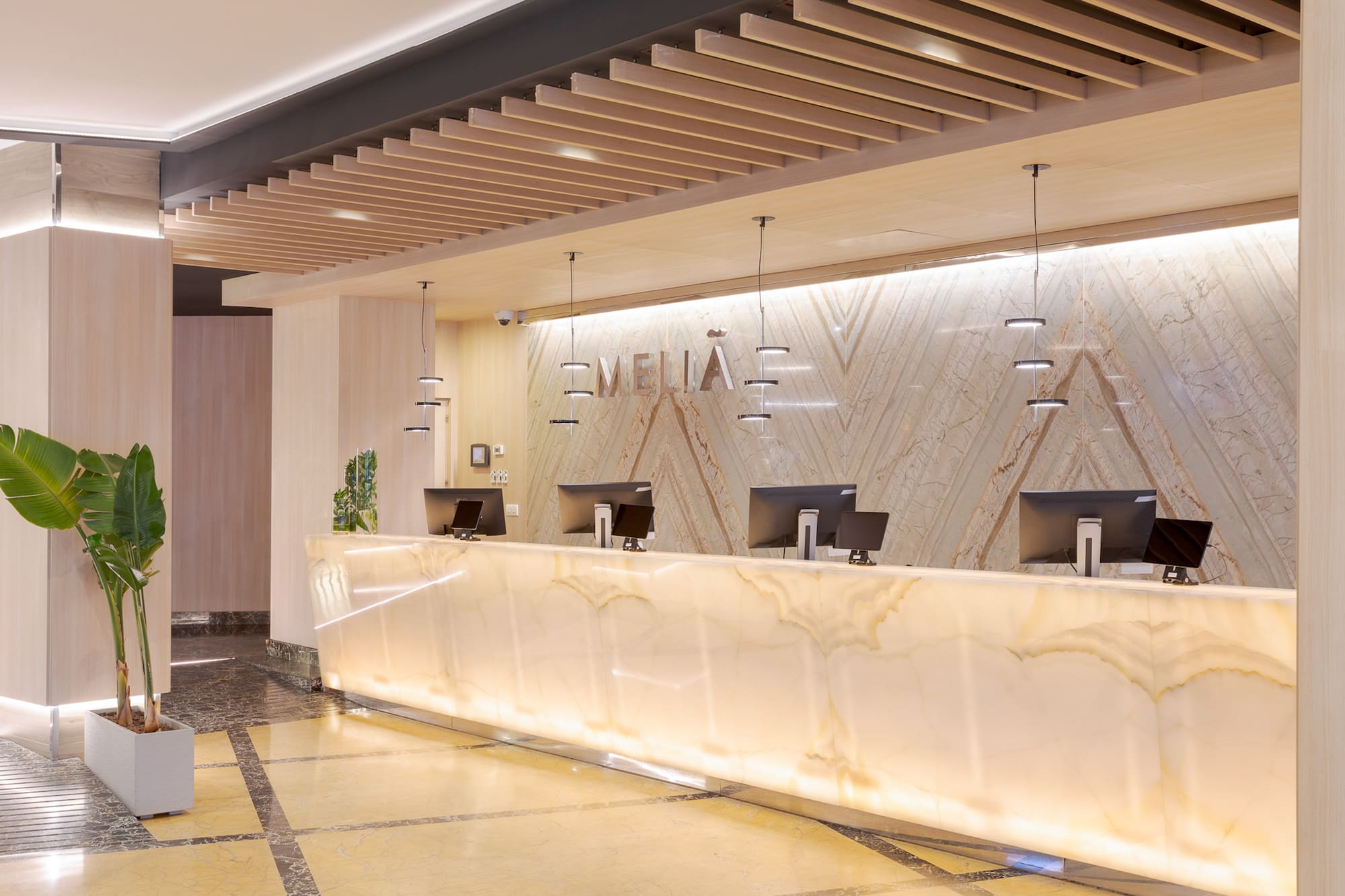 Meliá hotel front desk, glowing marble, modern design, wooden slat ceiling.