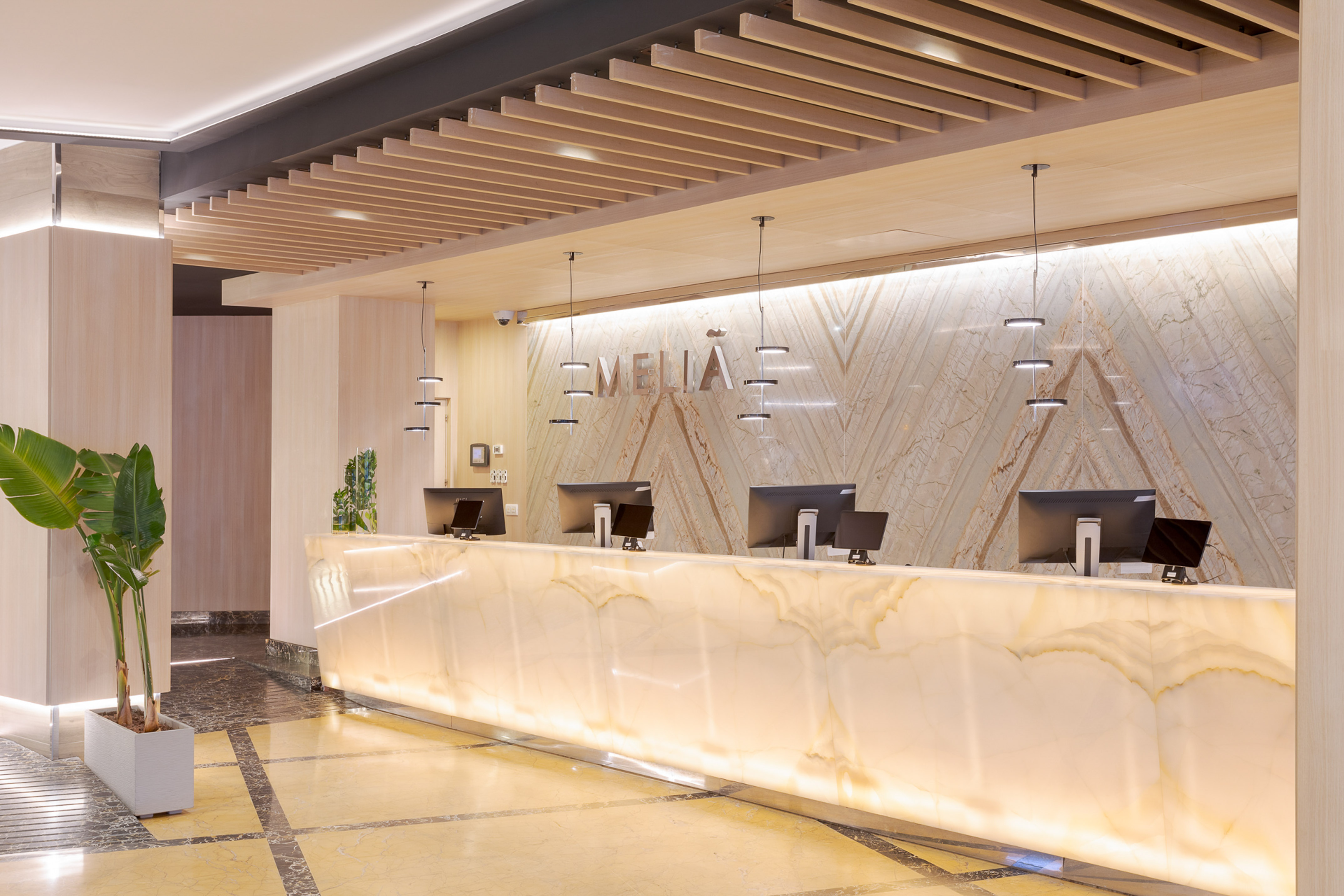 Meliá hotel front desk, glowing marble, modern design, wooden slat ceiling.