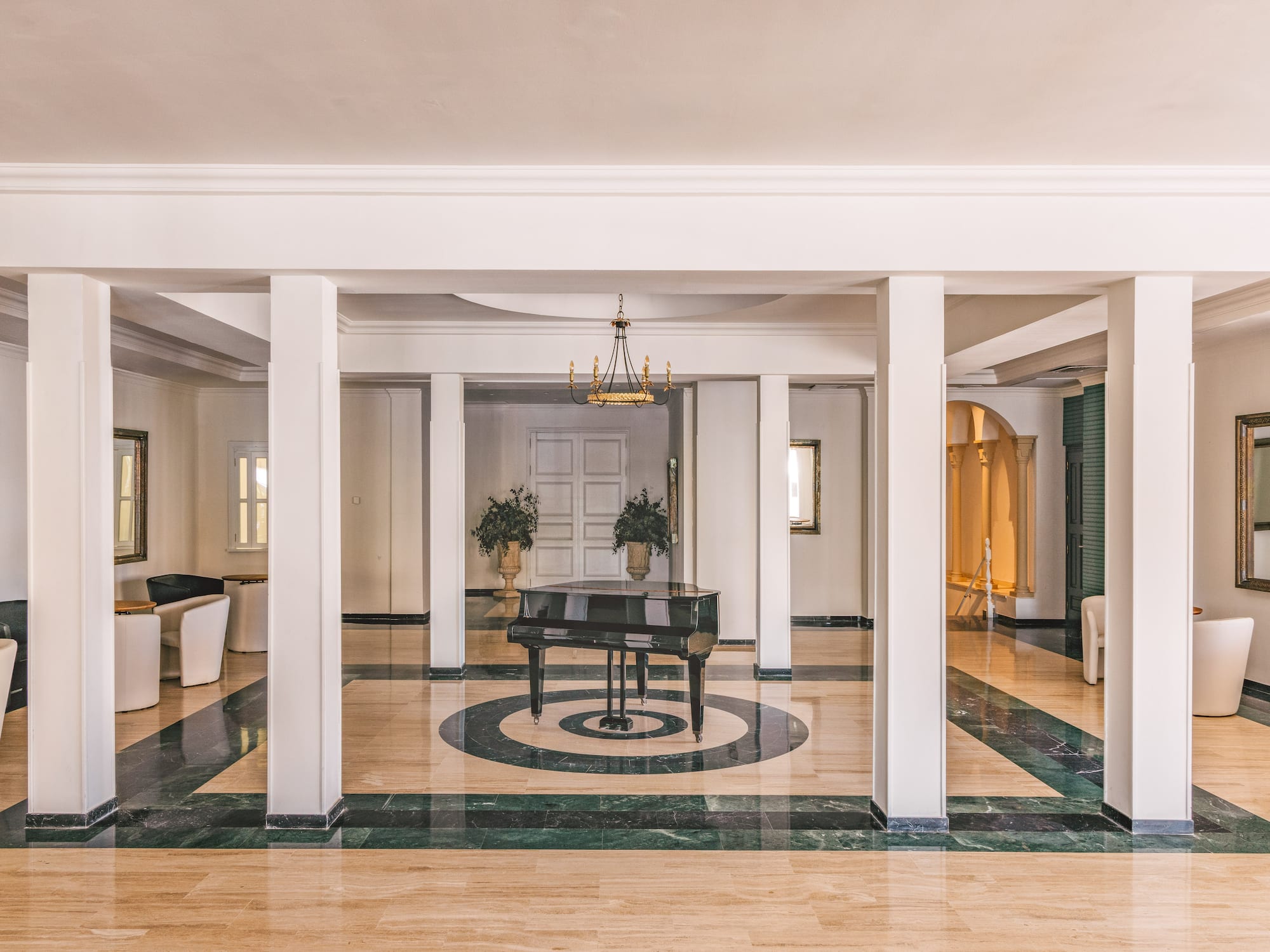Elegant hotel lobby with grand piano, marble floor, white pillars, and chandelier.