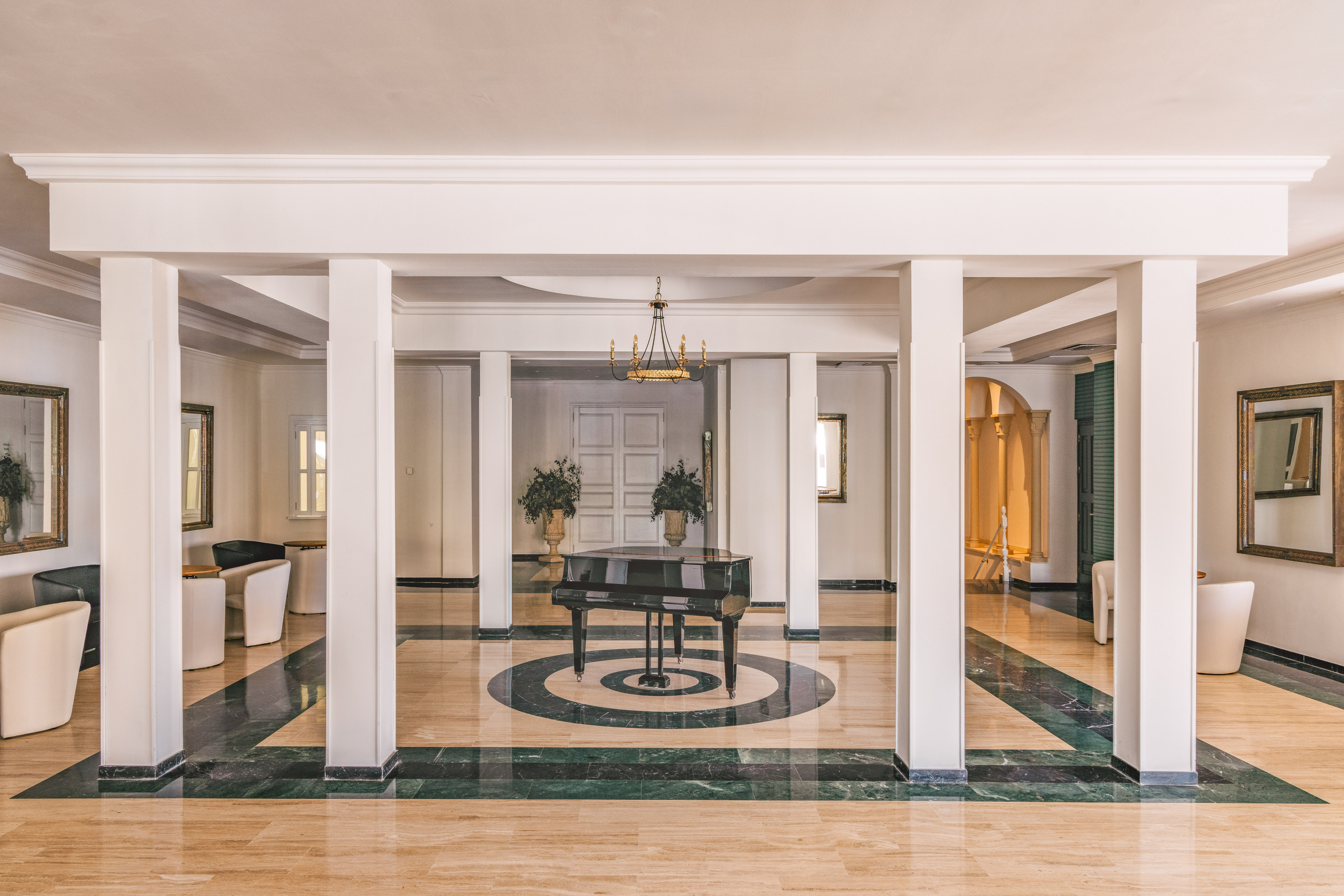 Elegant hotel lobby with grand piano, marble floor, white pillars, and chandelier.