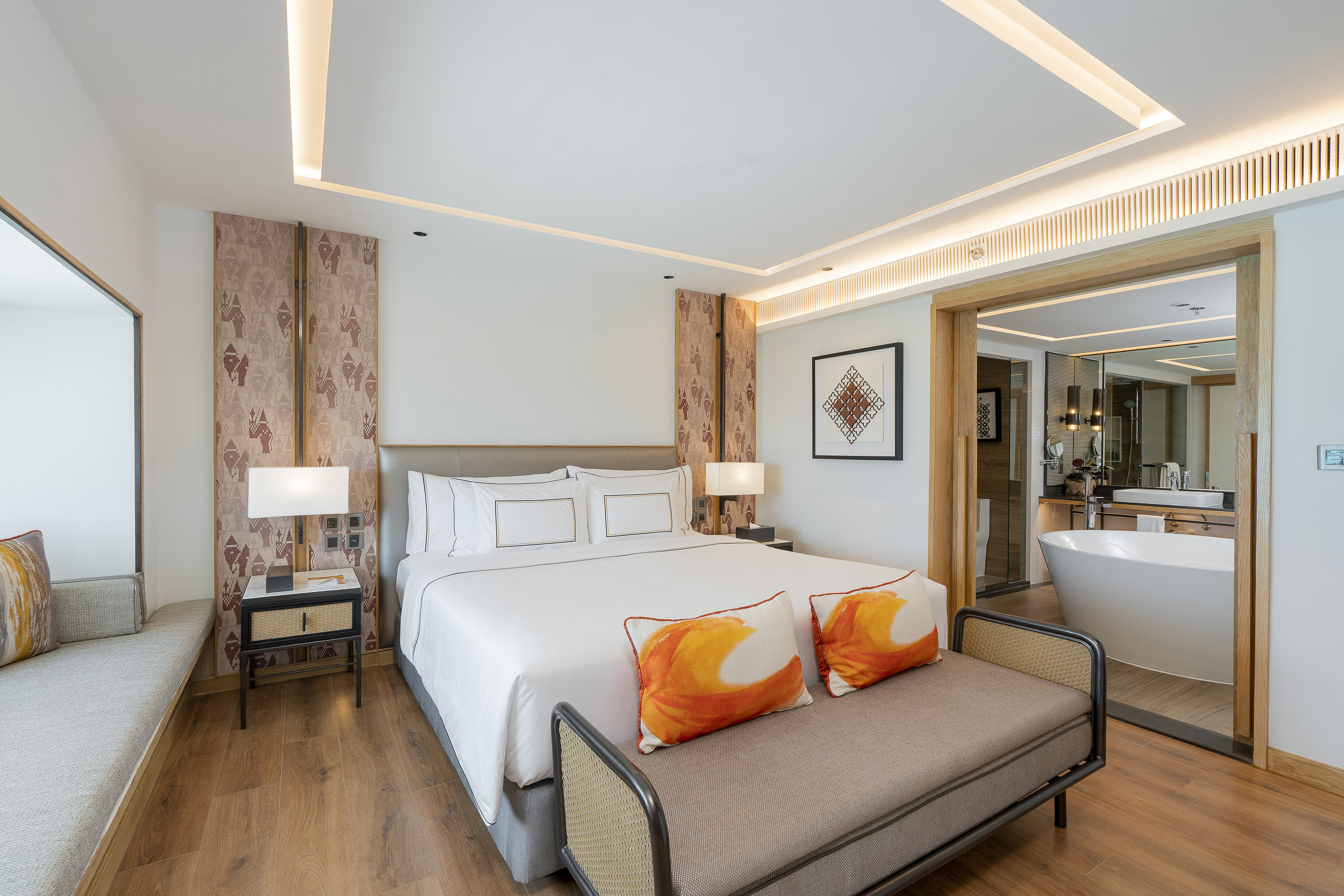 Modern luxury hotel bedroom with king bed, orange accents, and ensuite bathroom.