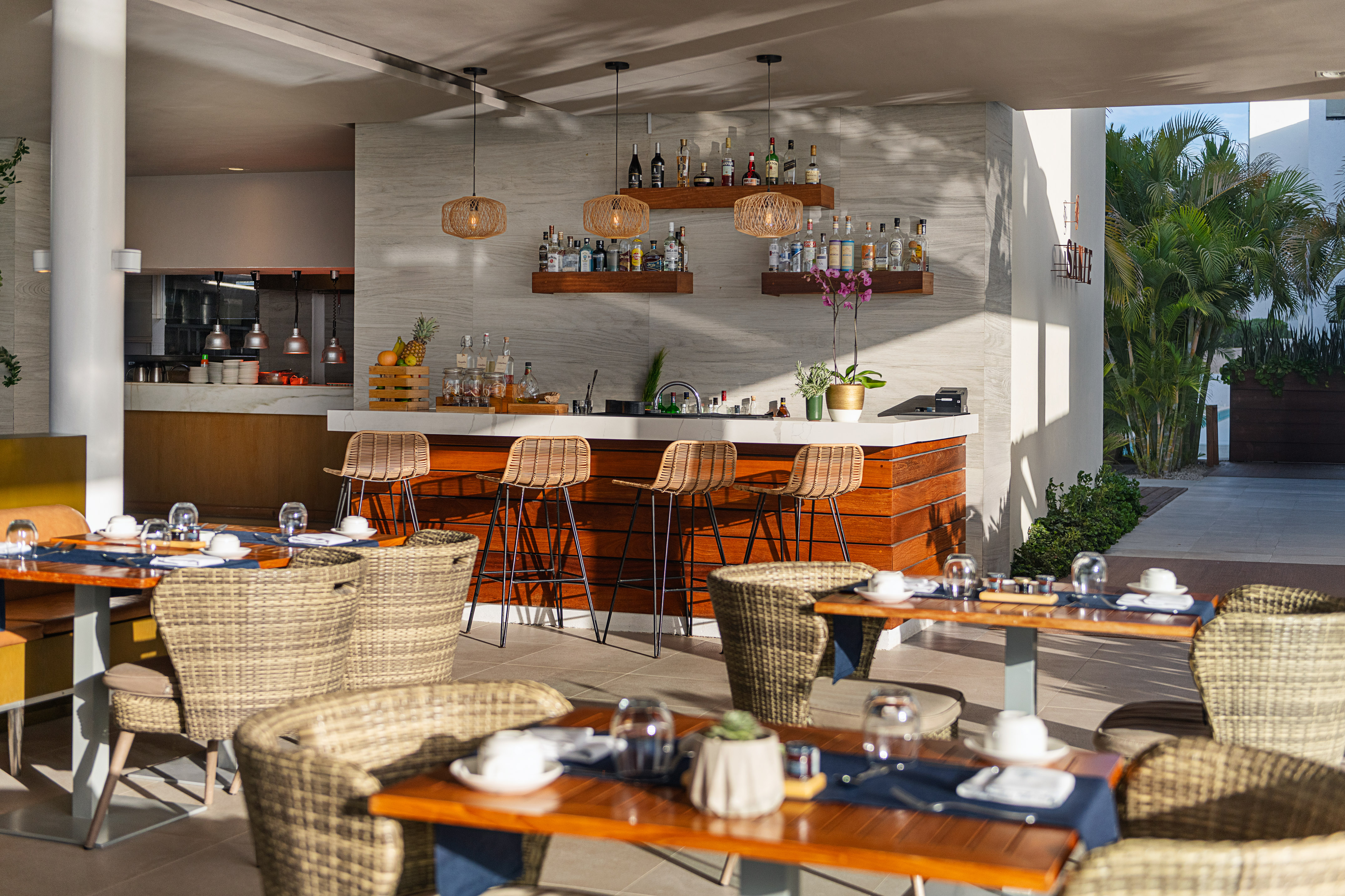 Tropical resort bar and outdoor dining area with wicker chairs and modern decor.
