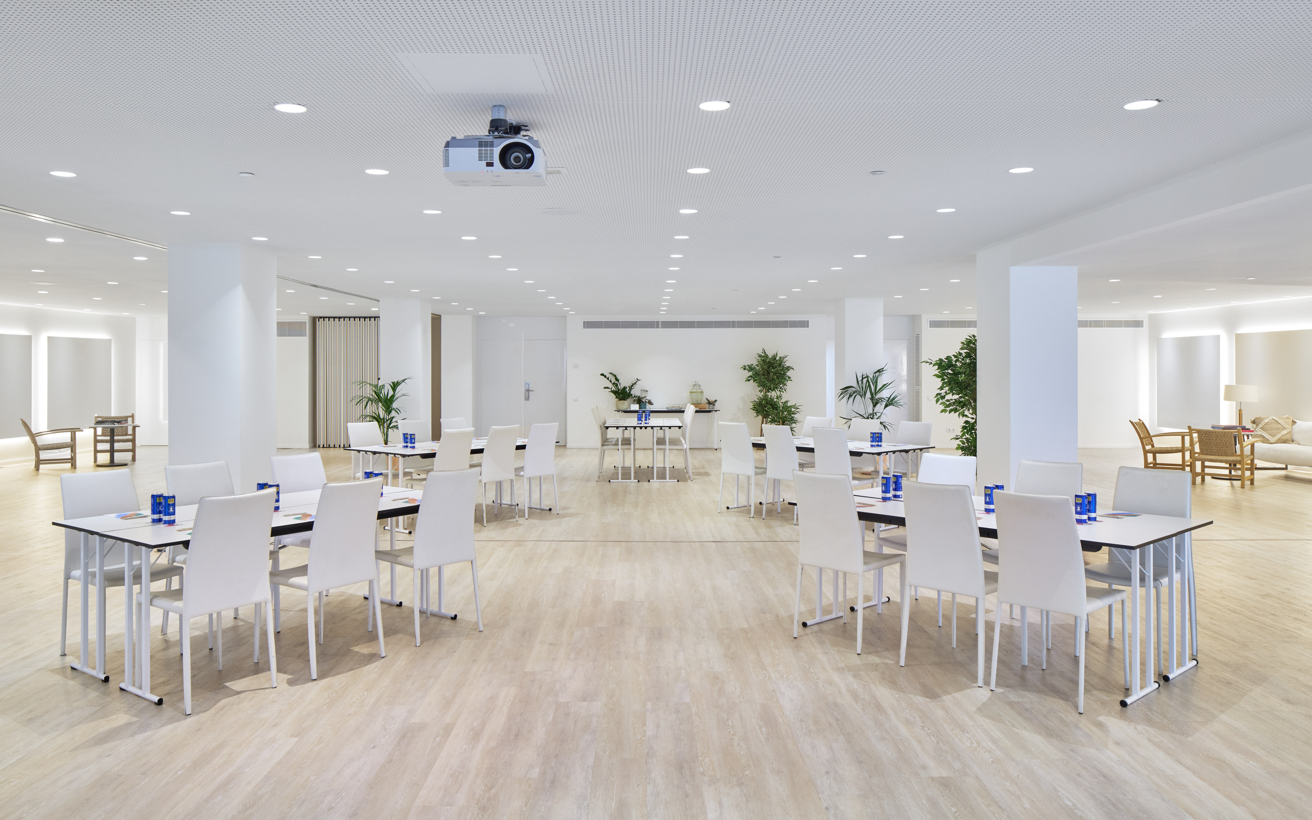 Modern conference room setup with white tables, chairs, and ceiling projector.