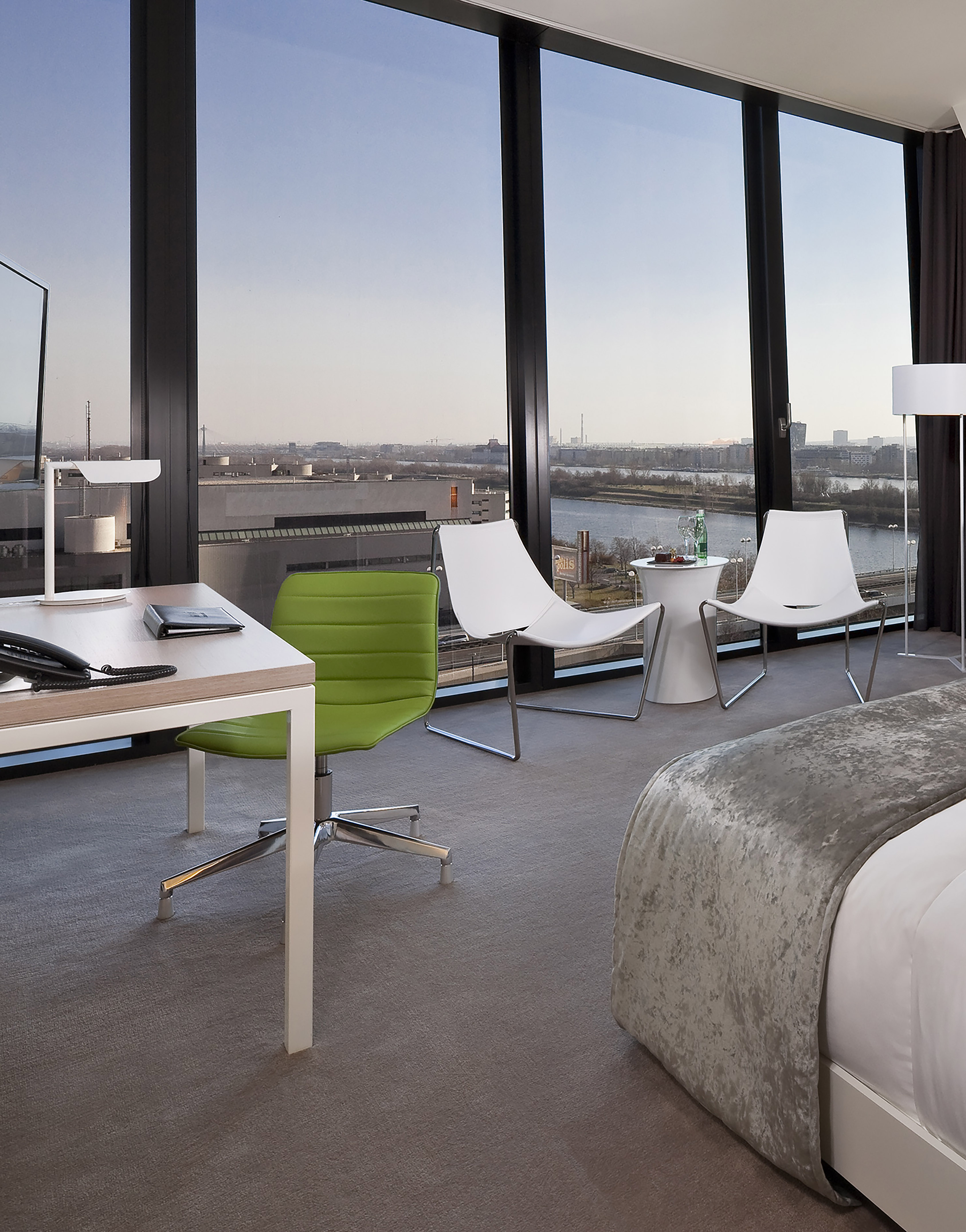 Modern hotel room with desk, green chair, and scenic river city view.