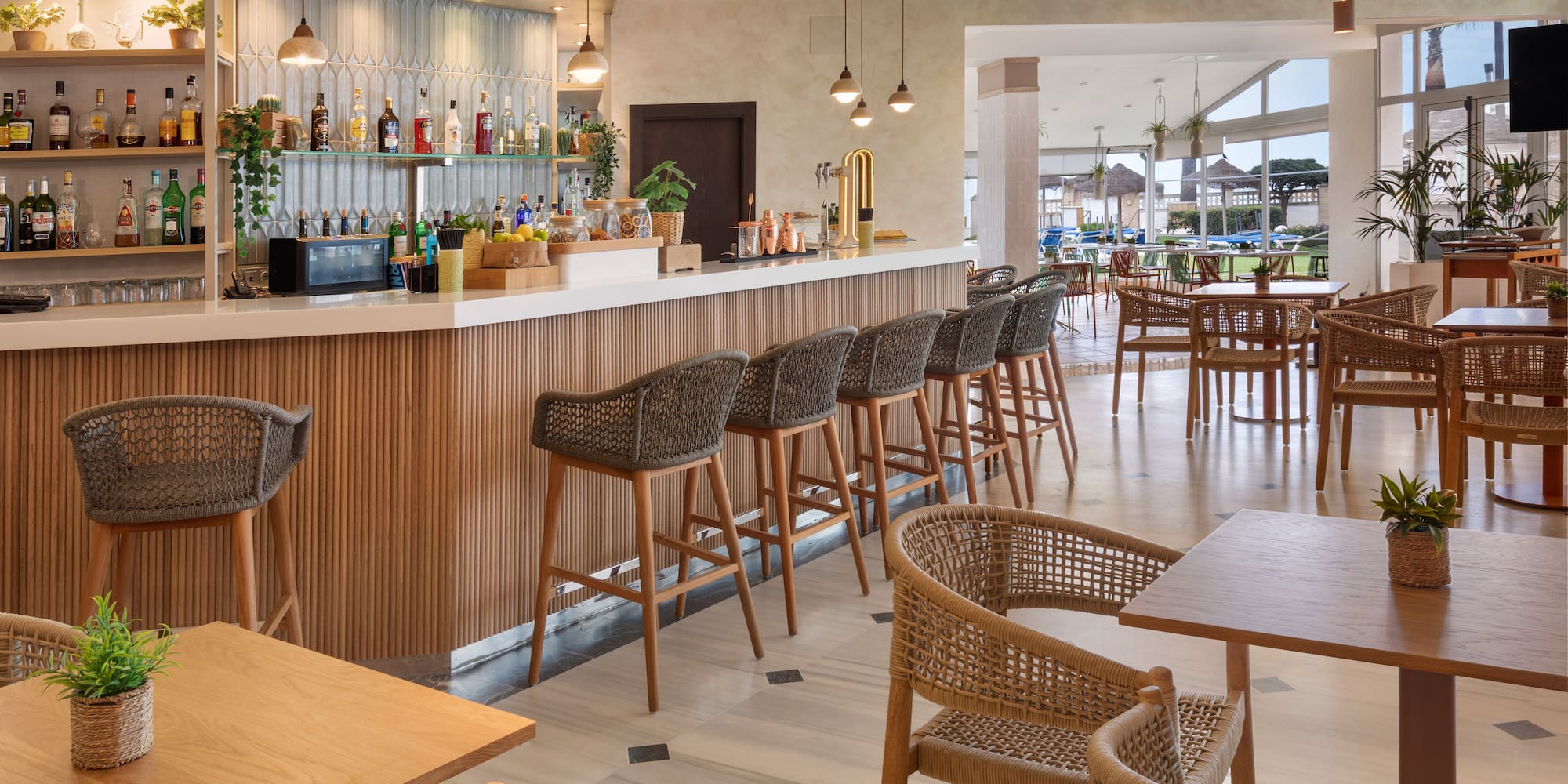 Bar de hotel moderno con mostrador, taburetes y mesas de restaurante.