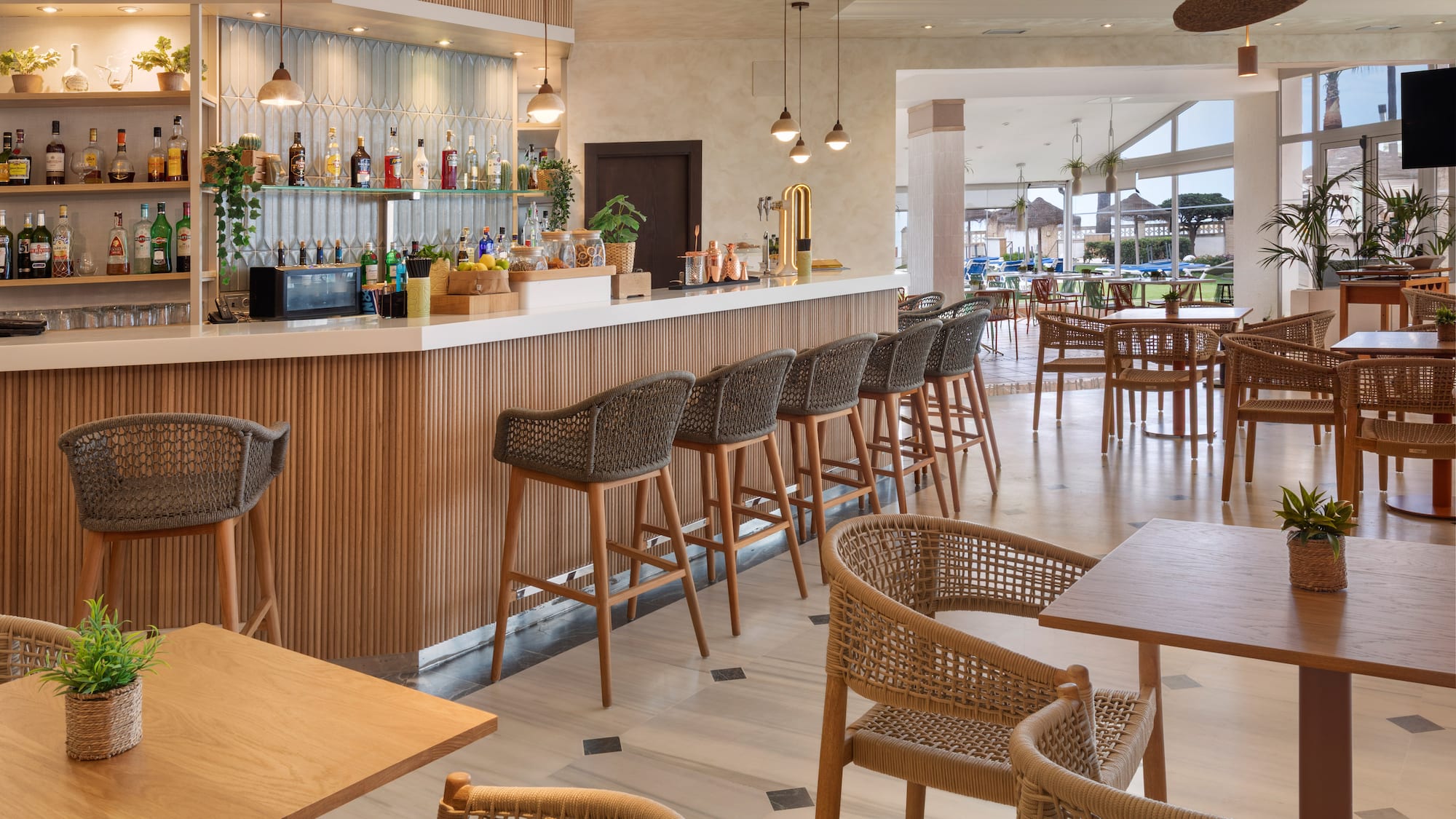 Bar de hotel moderno con mostrador, taburetes y mesas de restaurante.