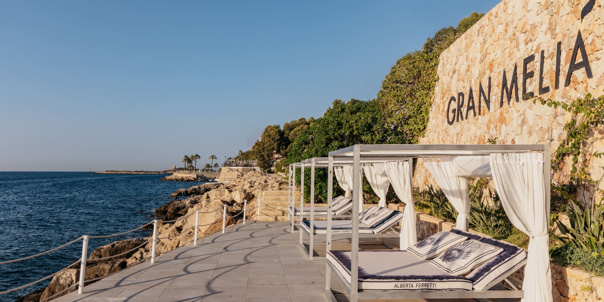 a group of beds on a deck next to a wall with trees and a sign.