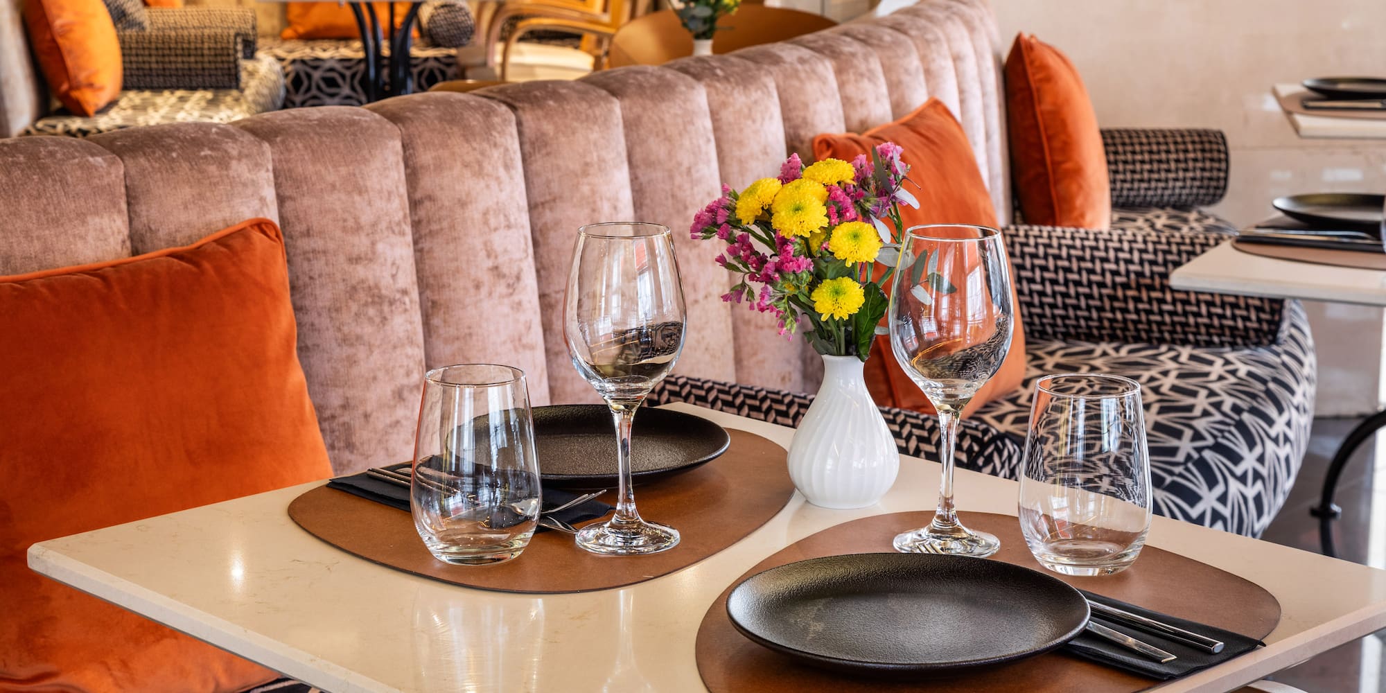 Elegant restaurant dining table set for two, colorful flowers, velvet banquette.