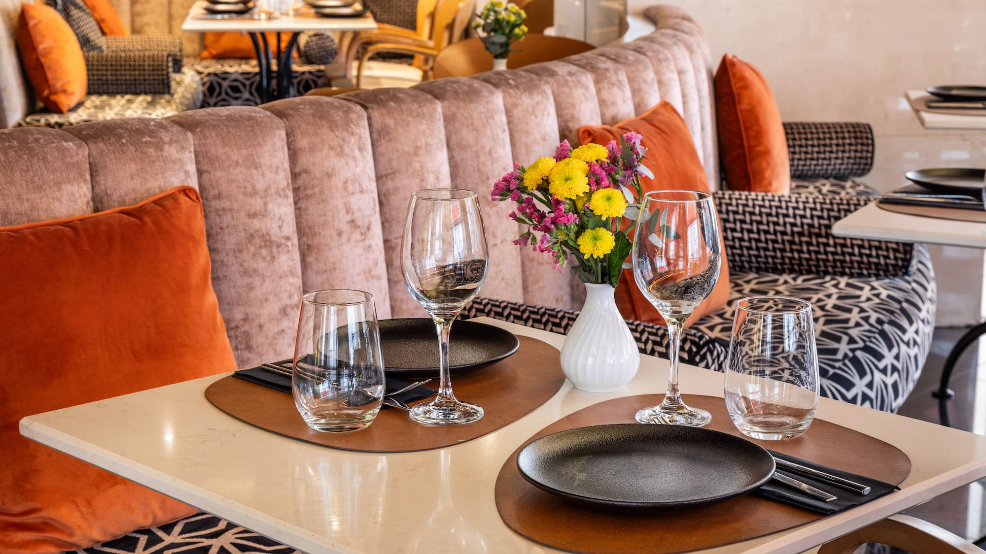 Elegant restaurant dining table set for two, colorful flowers, velvet banquette.