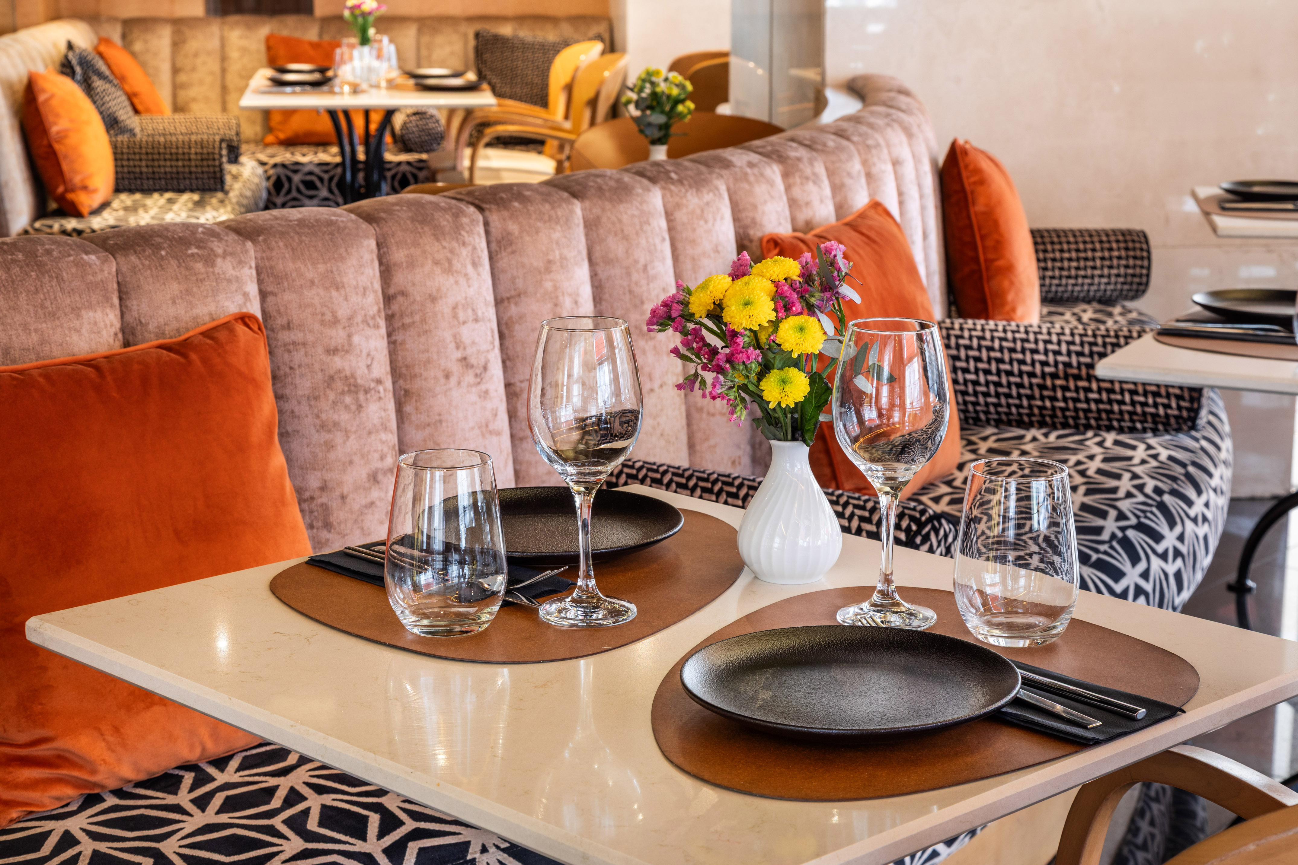 Elegant restaurant dining table set for two, colorful flowers, velvet banquette.