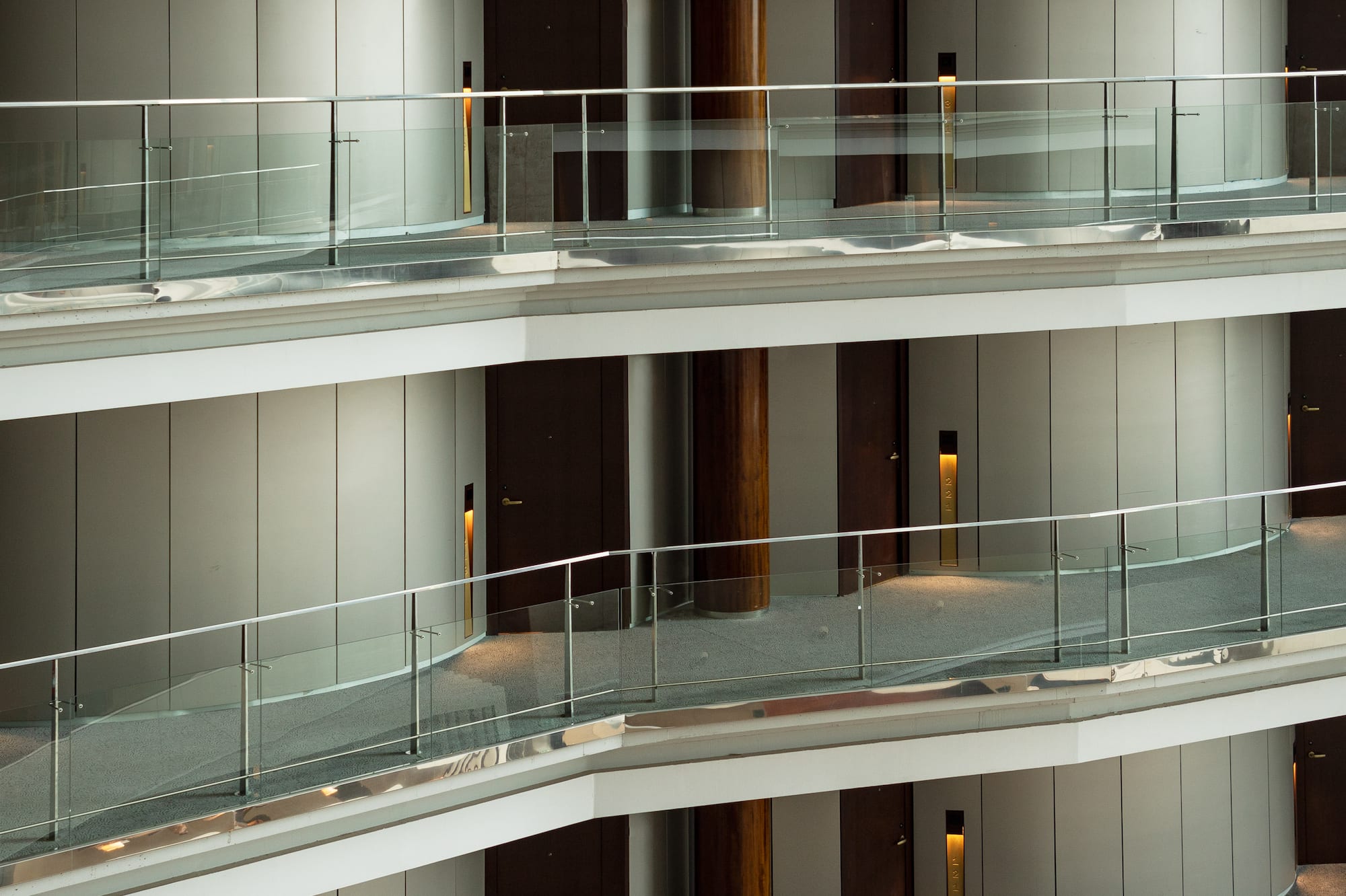 Modern hotel atrium with multi-level corridors, glass railings, and dark doors.