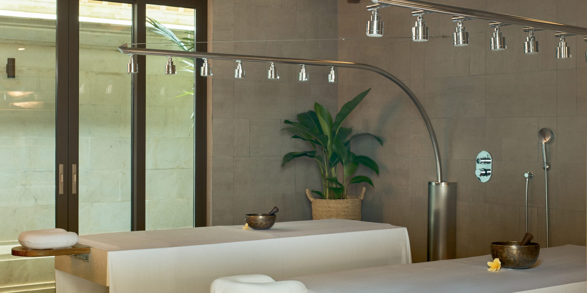 Luxury spa massage room with two beds, rain shower, and tropical plant.