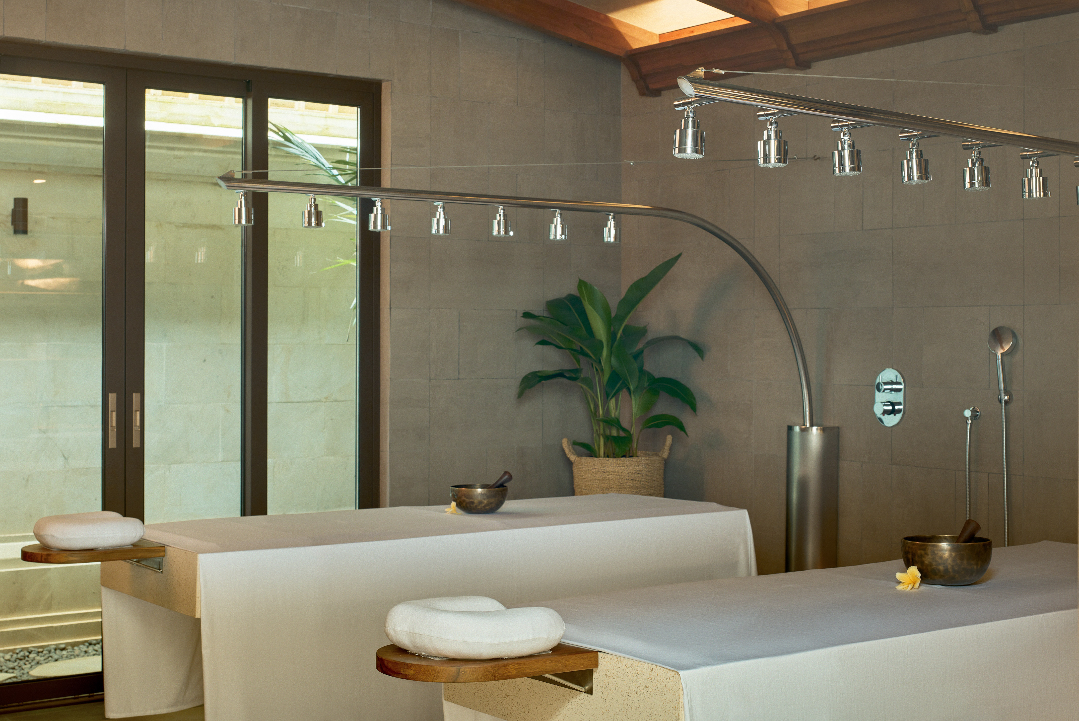 Luxury spa massage room with two beds, rain shower, and tropical plant.