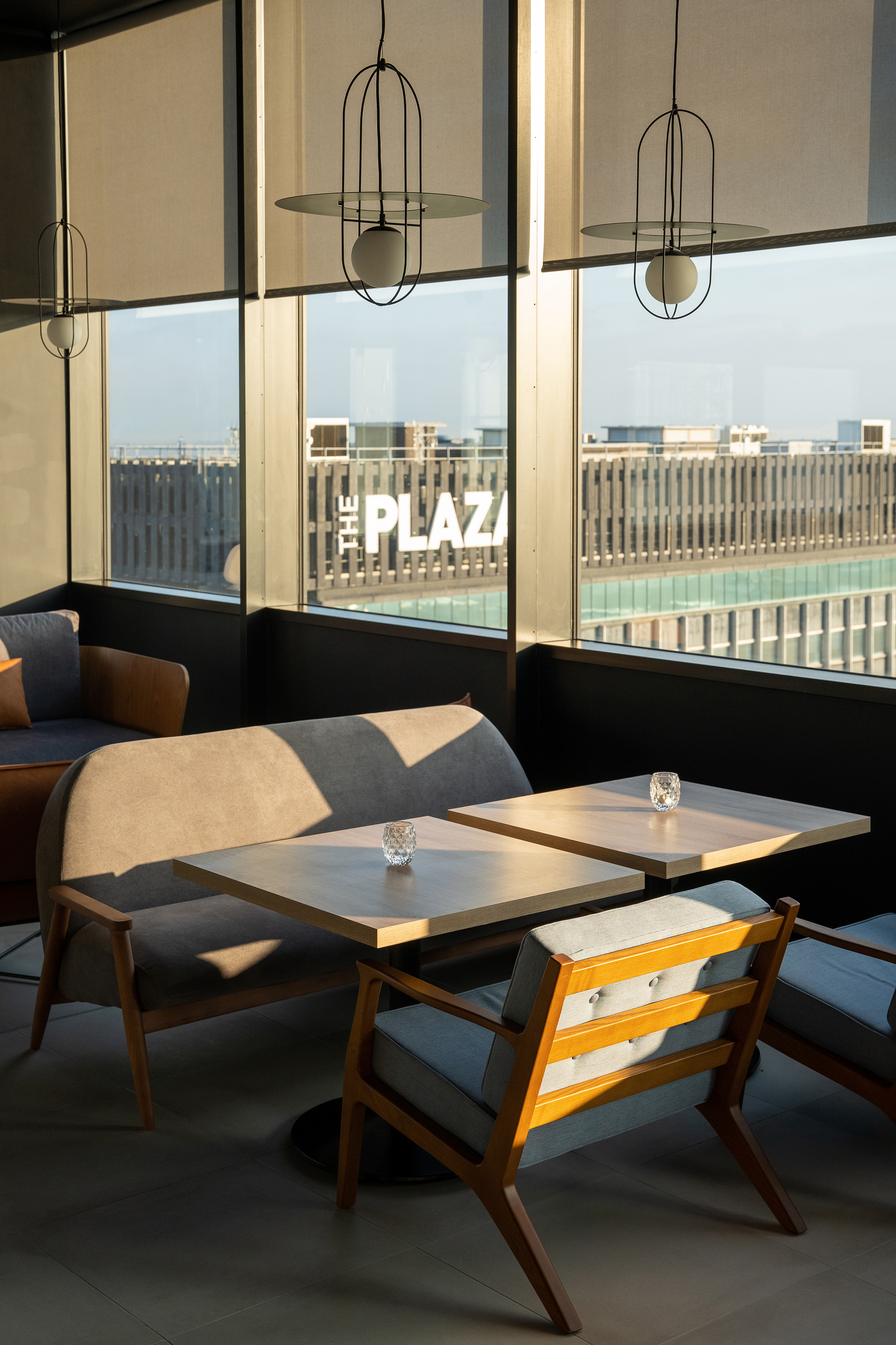 Modern cafe lounge with city view, sunlit tables, and contemporary seating.