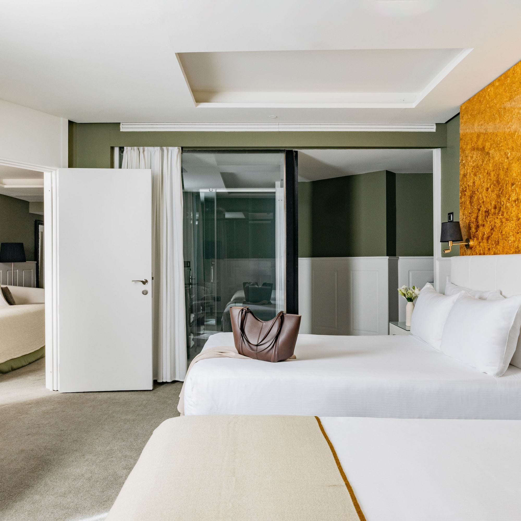 Habitación de hotel moderna con camas, paredes verdes y acento dorado.