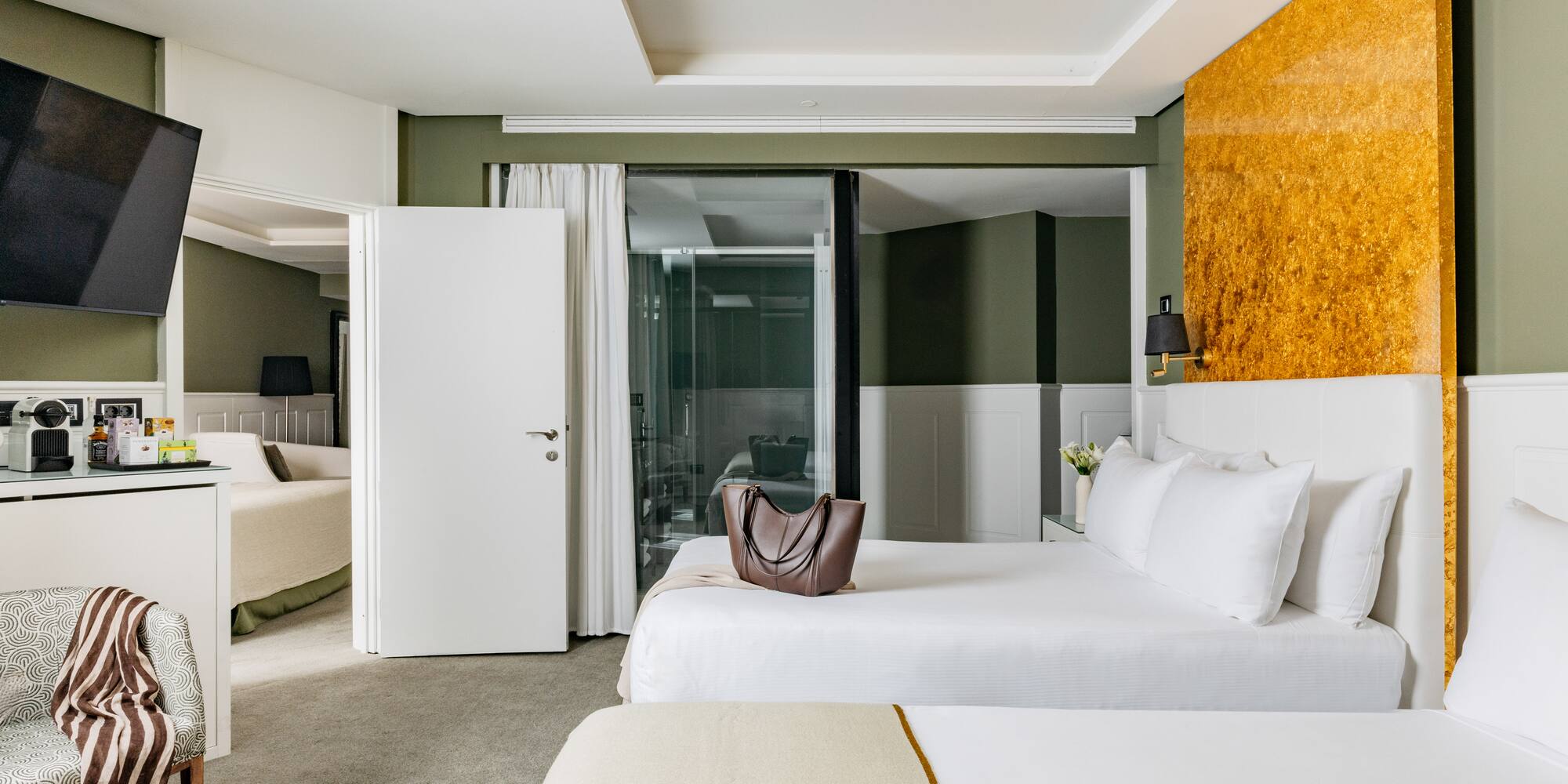 Habitación de hotel moderna con camas, paredes verdes y acento dorado.