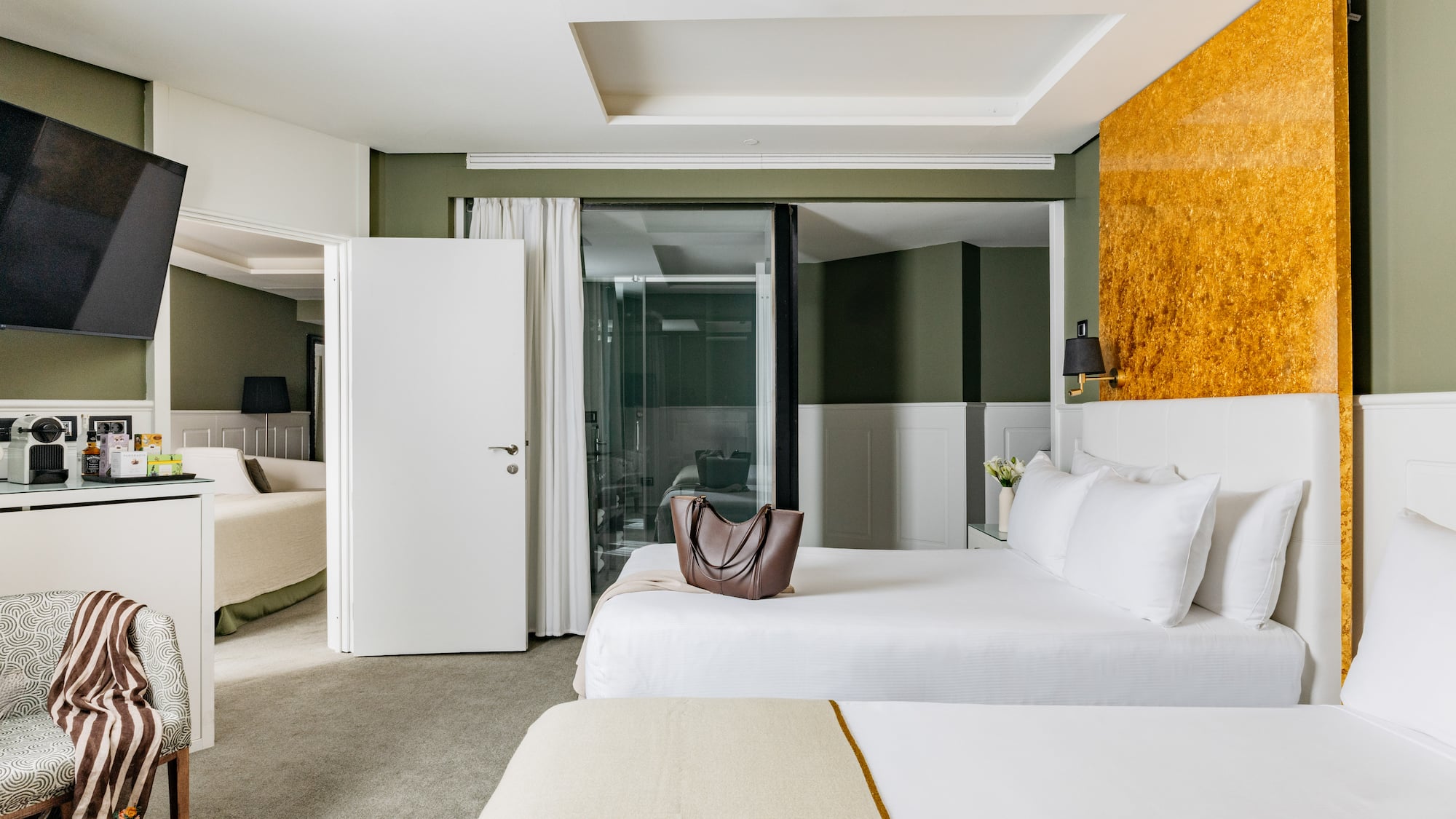 Habitación de hotel moderna con camas, paredes verdes y acento dorado.