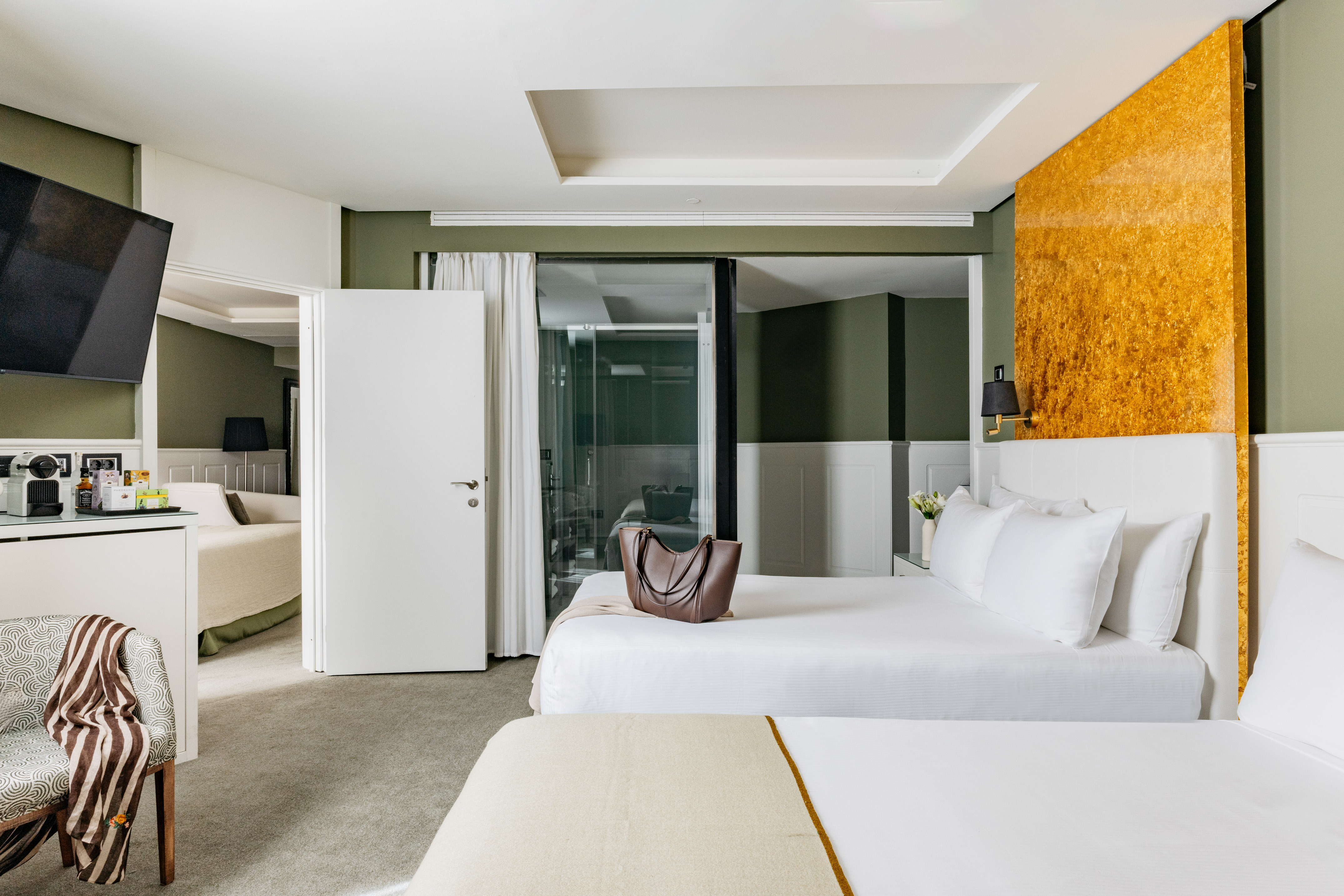 Habitación de hotel moderna con camas, paredes verdes y acento dorado.