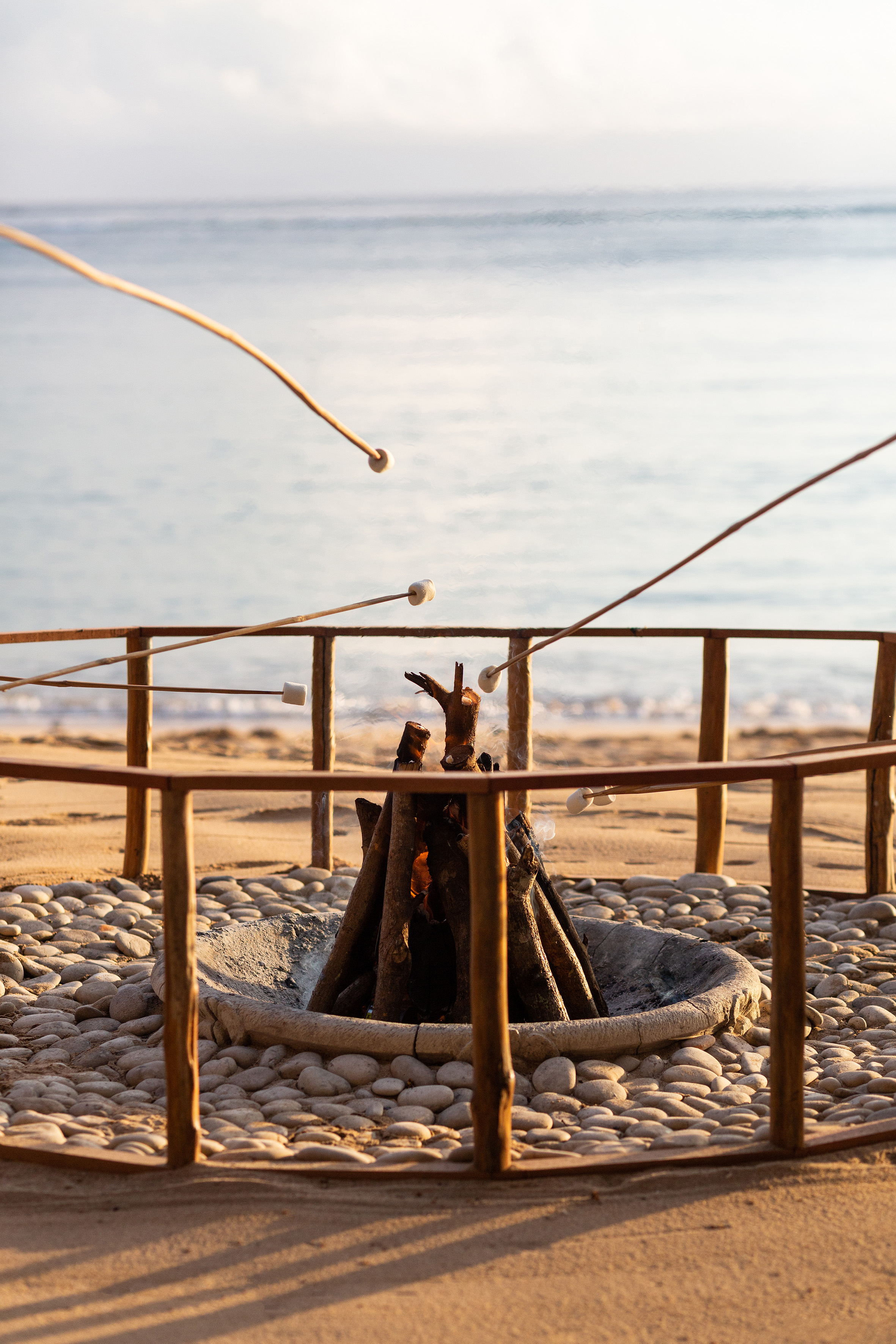 Roasting marshmallows over a beach bonfire at sunset by the ocean.