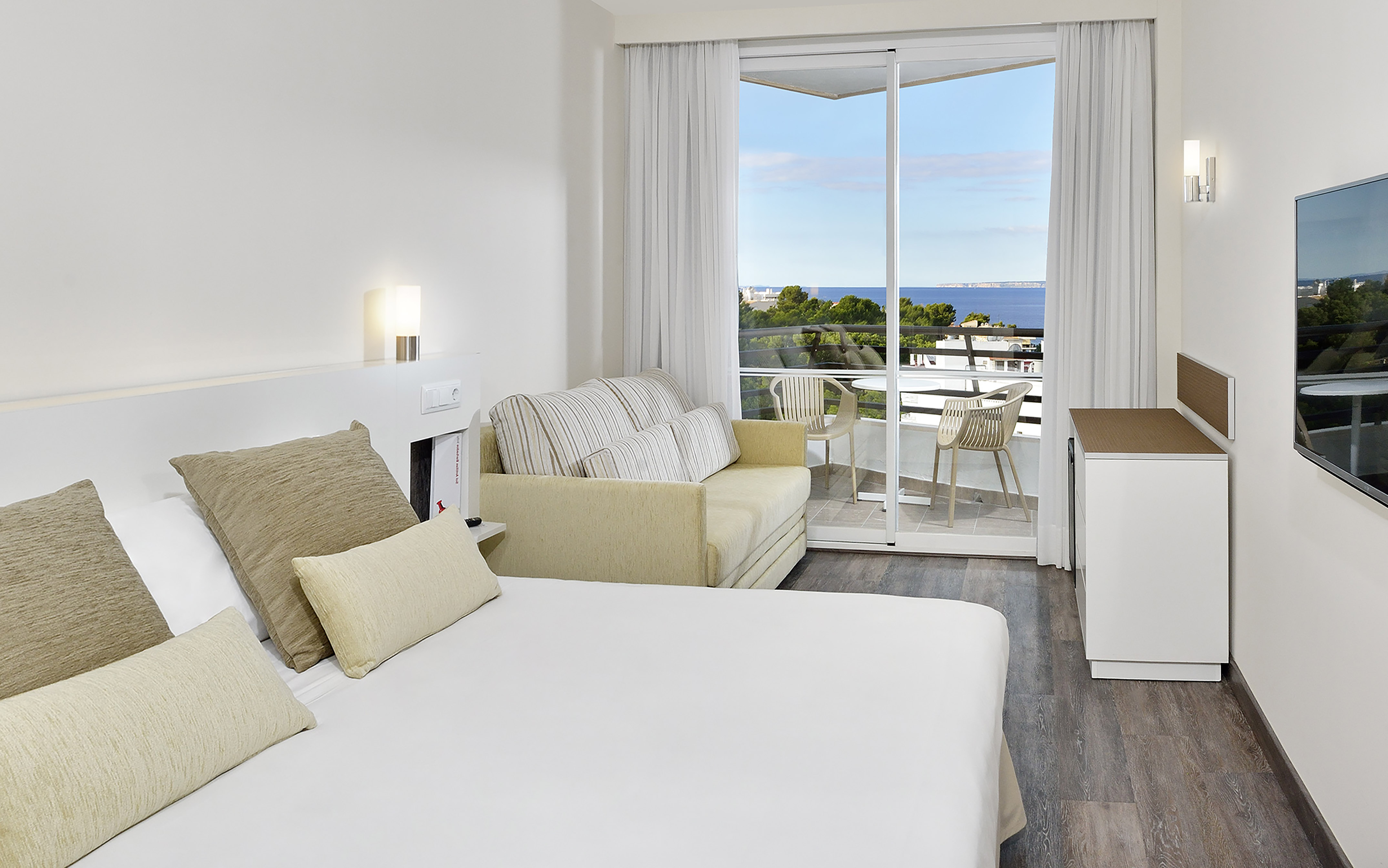 Bright hotel room with ocean view balcony, bed, and sofa.